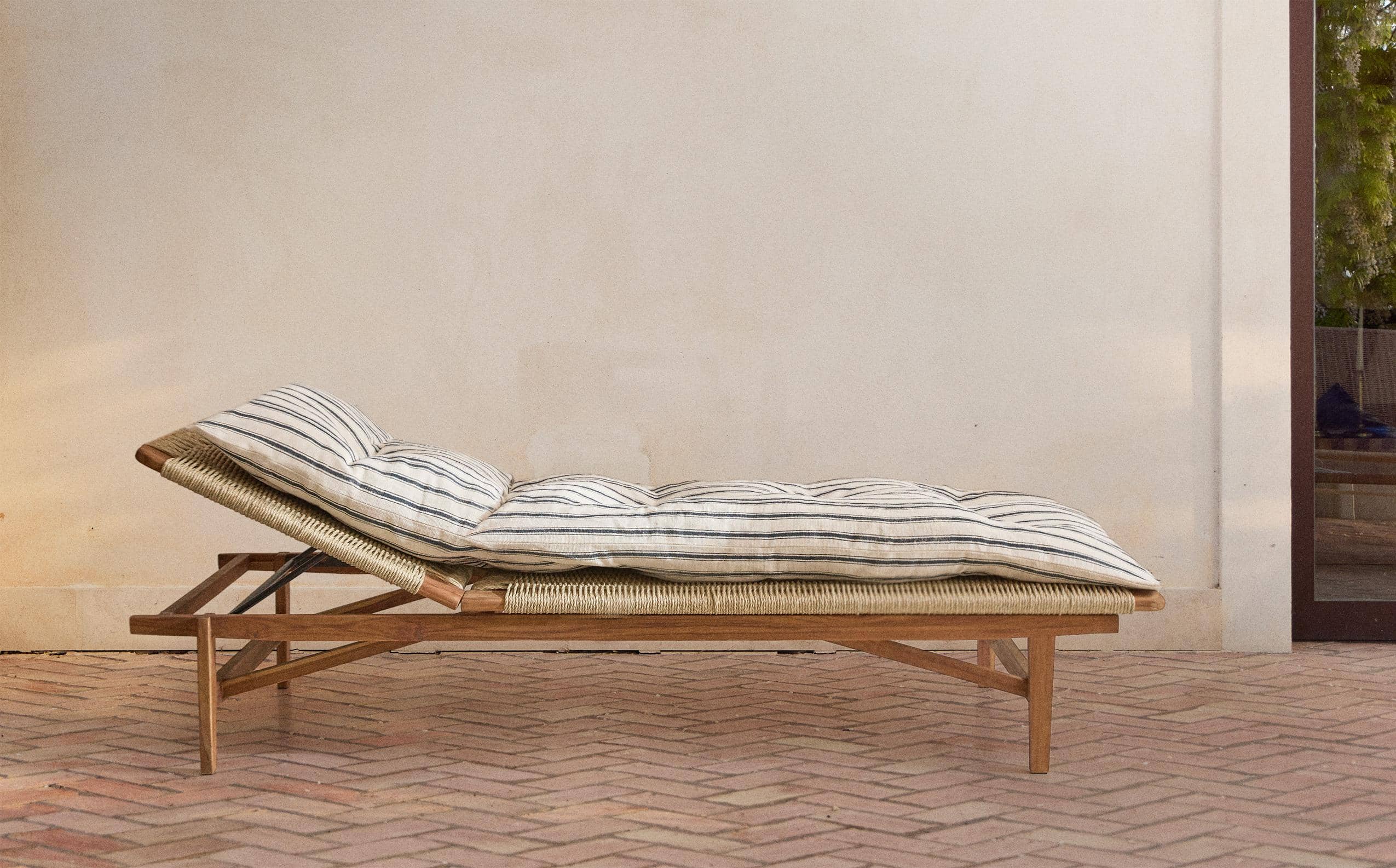 Full side view of the Cord lounger on a herringbone brick terrace, with its back raised, woven cord seat, teak frame and striped cushion.