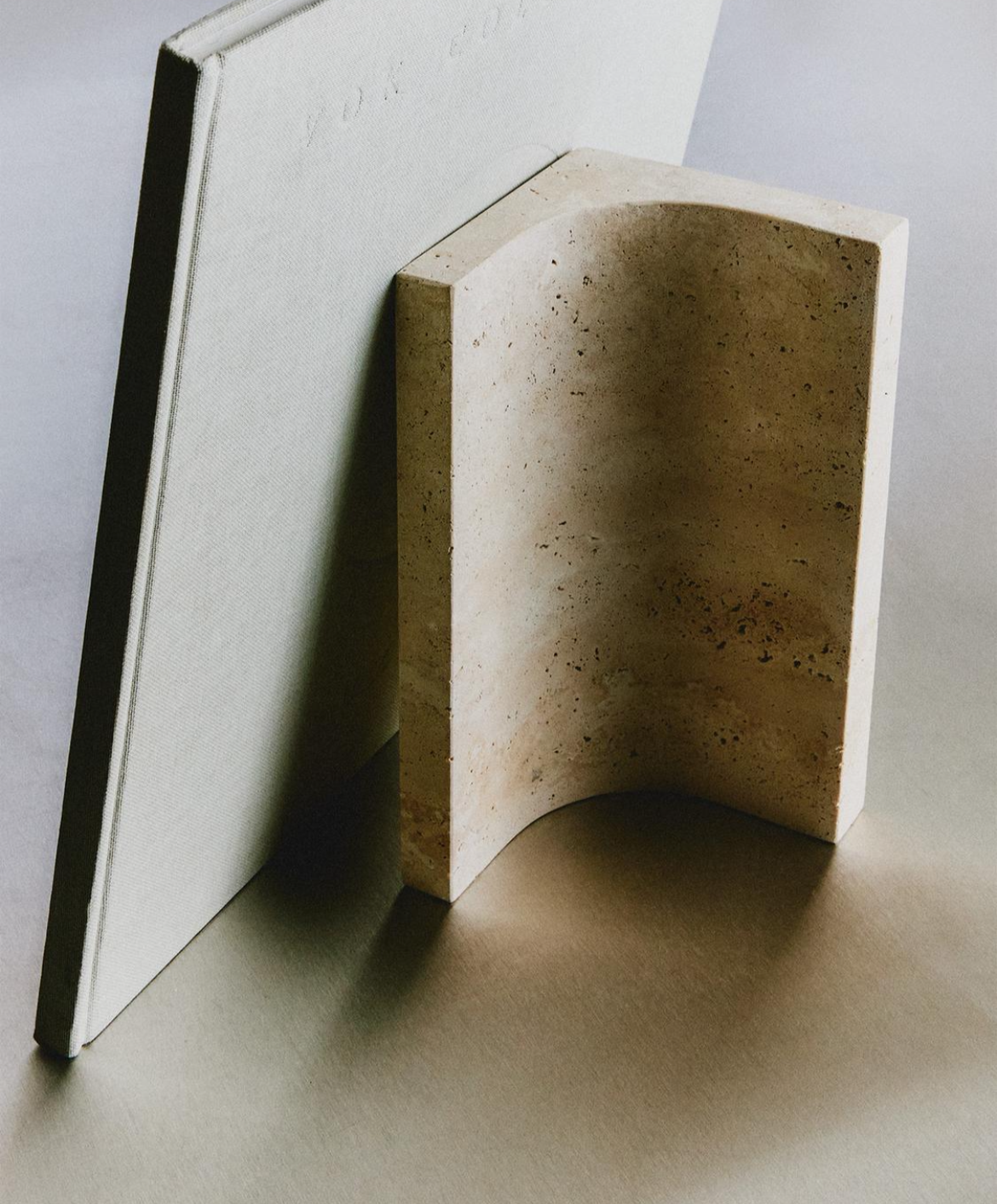 Tondo bookend at an angle against a large grey book, showing its smooth curved inner face and speckled surface.