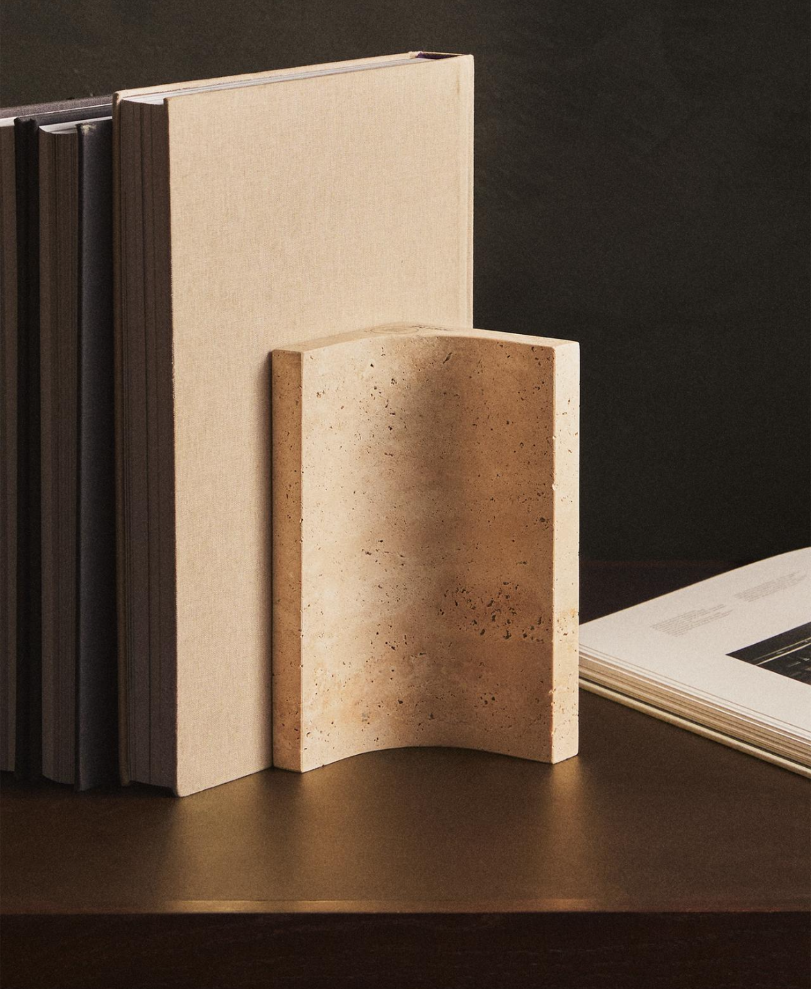 Tondo bookend holding a row of books, with a cream-covered book beside it and an open book at the edge, against a dark background.