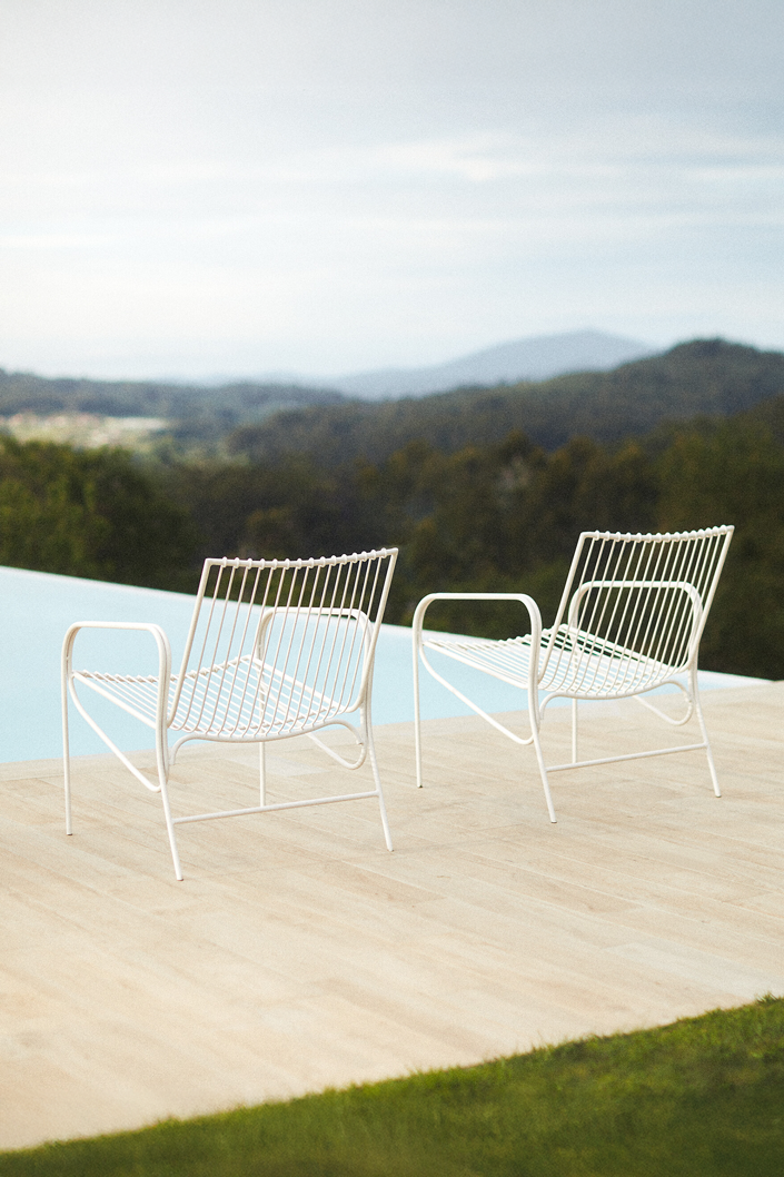 Two white Cala chairs with slatted backs on a stone terrace beside a pool