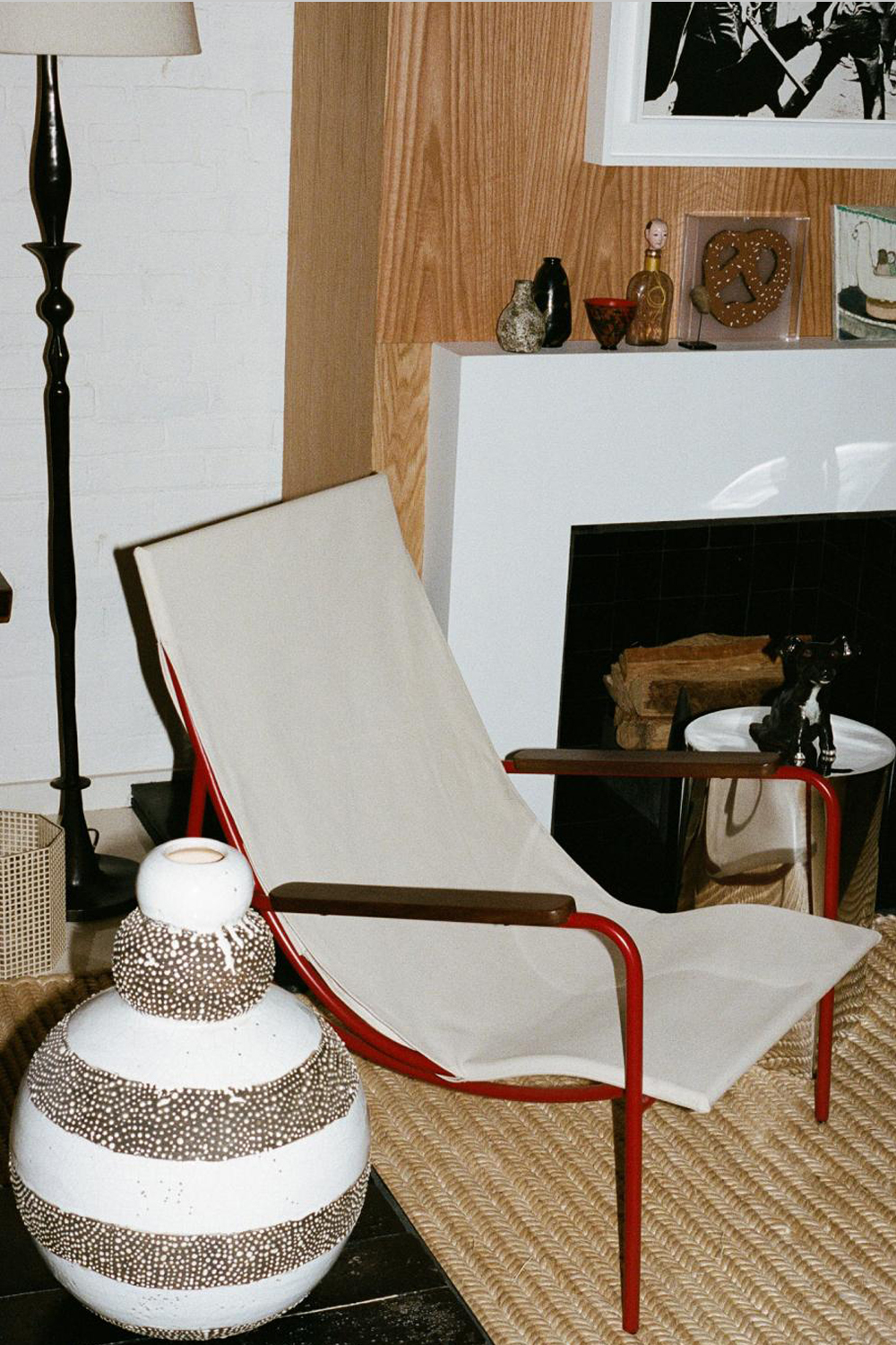 Tropico chair in a lived-in corner beside a white ceramic vase with brown dotted bands, on a woven rug in front of a fireplace.