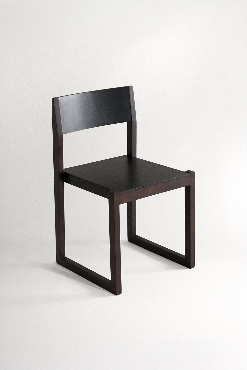 Ray chair at three-quarters on a plain light background, showing its dark wood sled frame, black leather seat and curved black backrest panel.