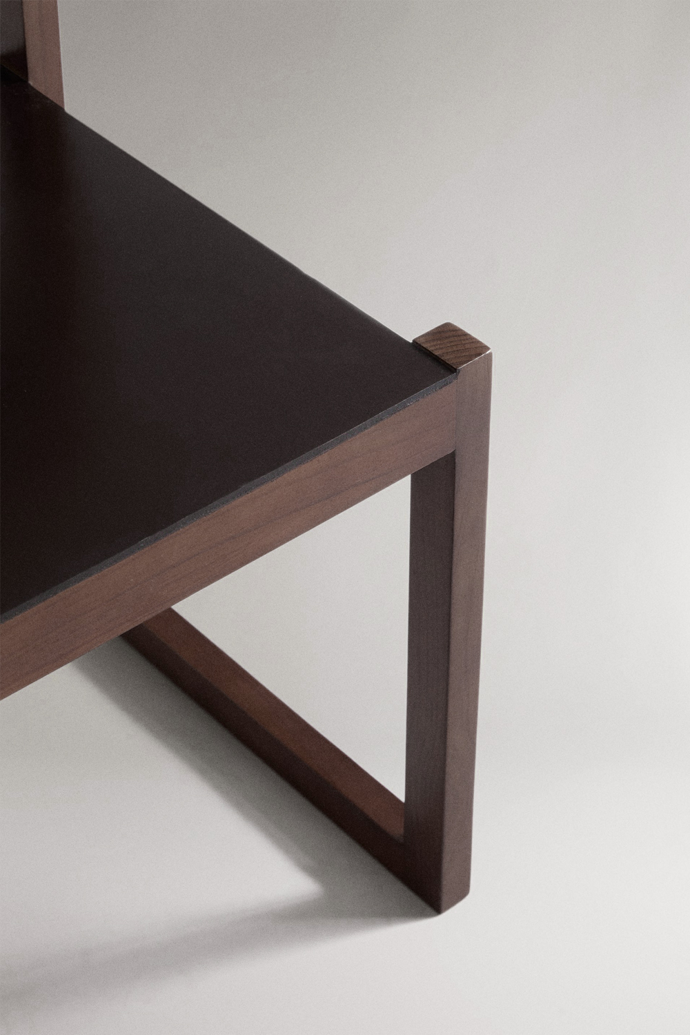 Close-up of the Ray chair's seat corner, showing the black leather seat edge, the dark wood joint and the sled leg.