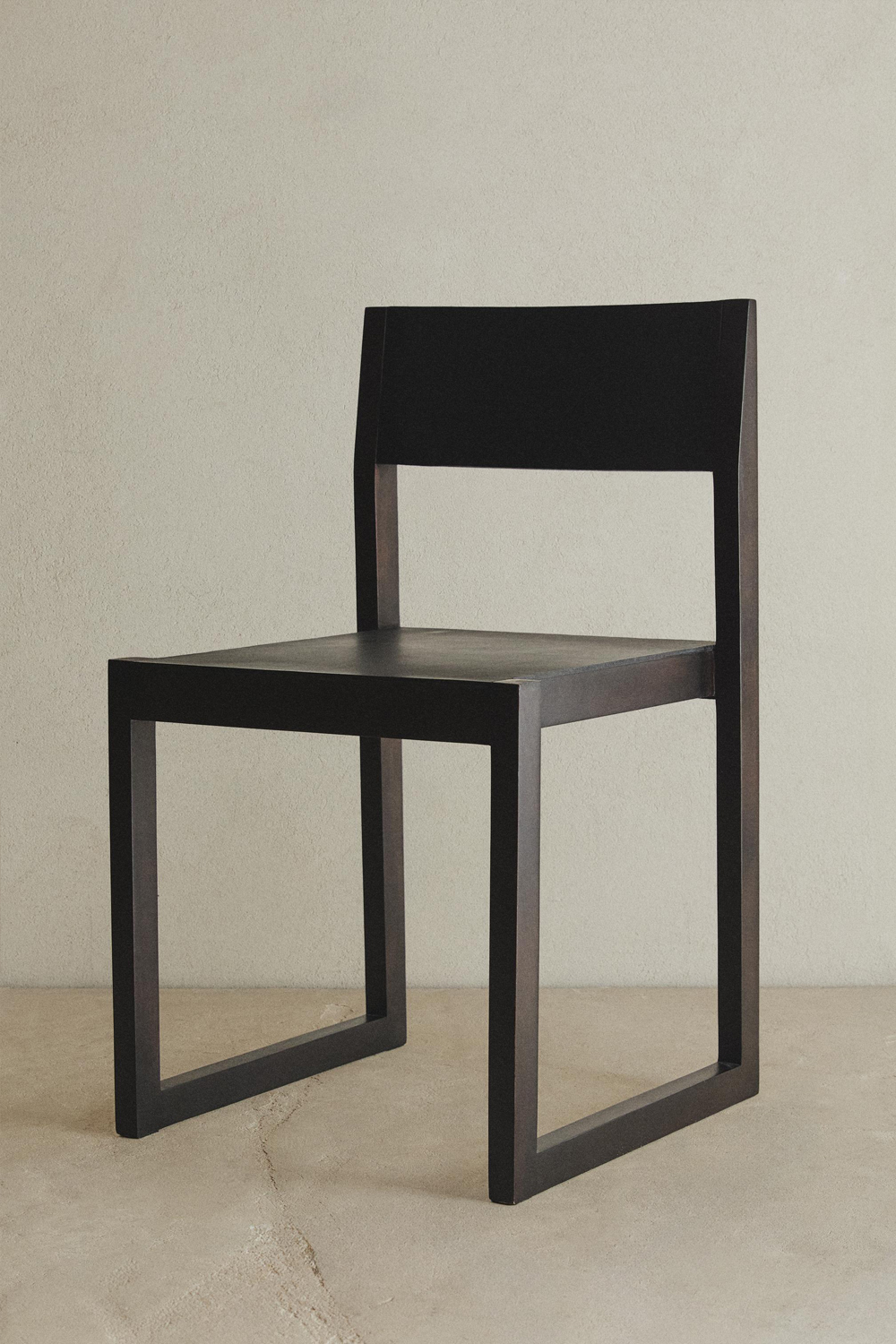 Ray chair on a pale concrete floor against a stone-coloured wall, with a dark frame and black leather seat and backrest.