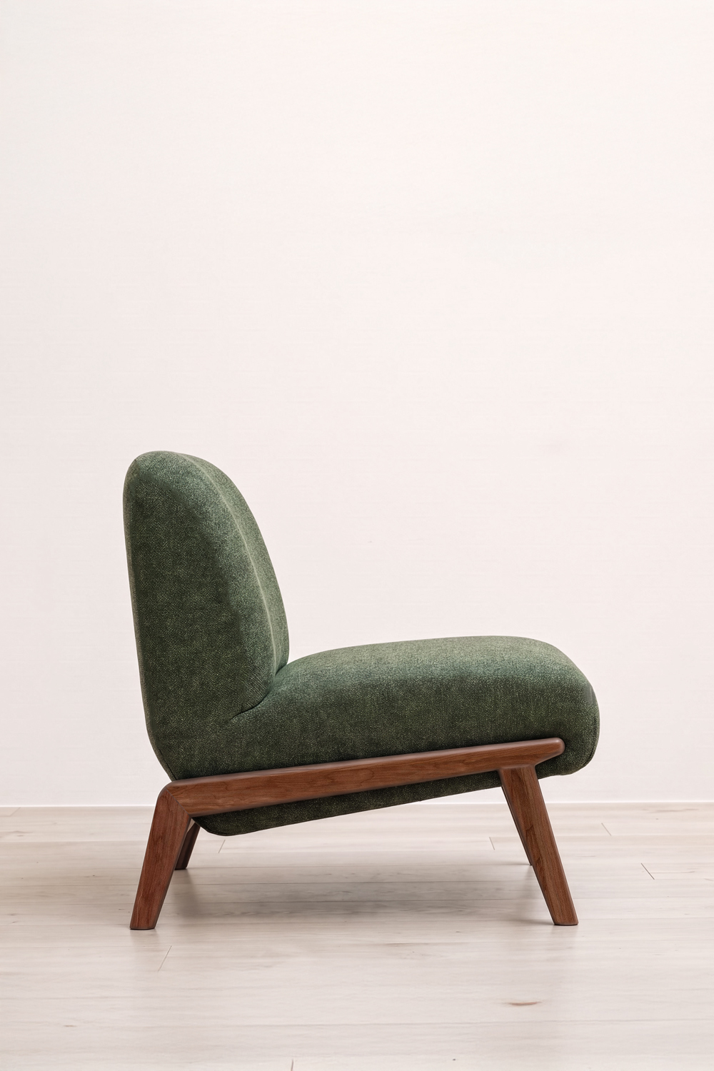 Side profile of the green Camilla chair, with its tall rounded back, deep seat and dark wood frame on a light wood floor.