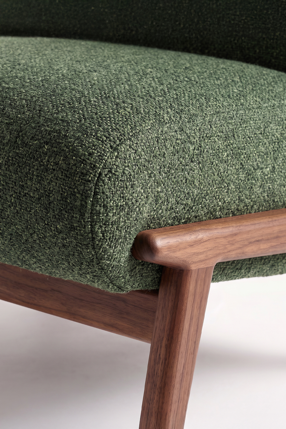 Close-up of the green seat edge, showing the nubby woven fabric and the rounded walnut frame and leg.