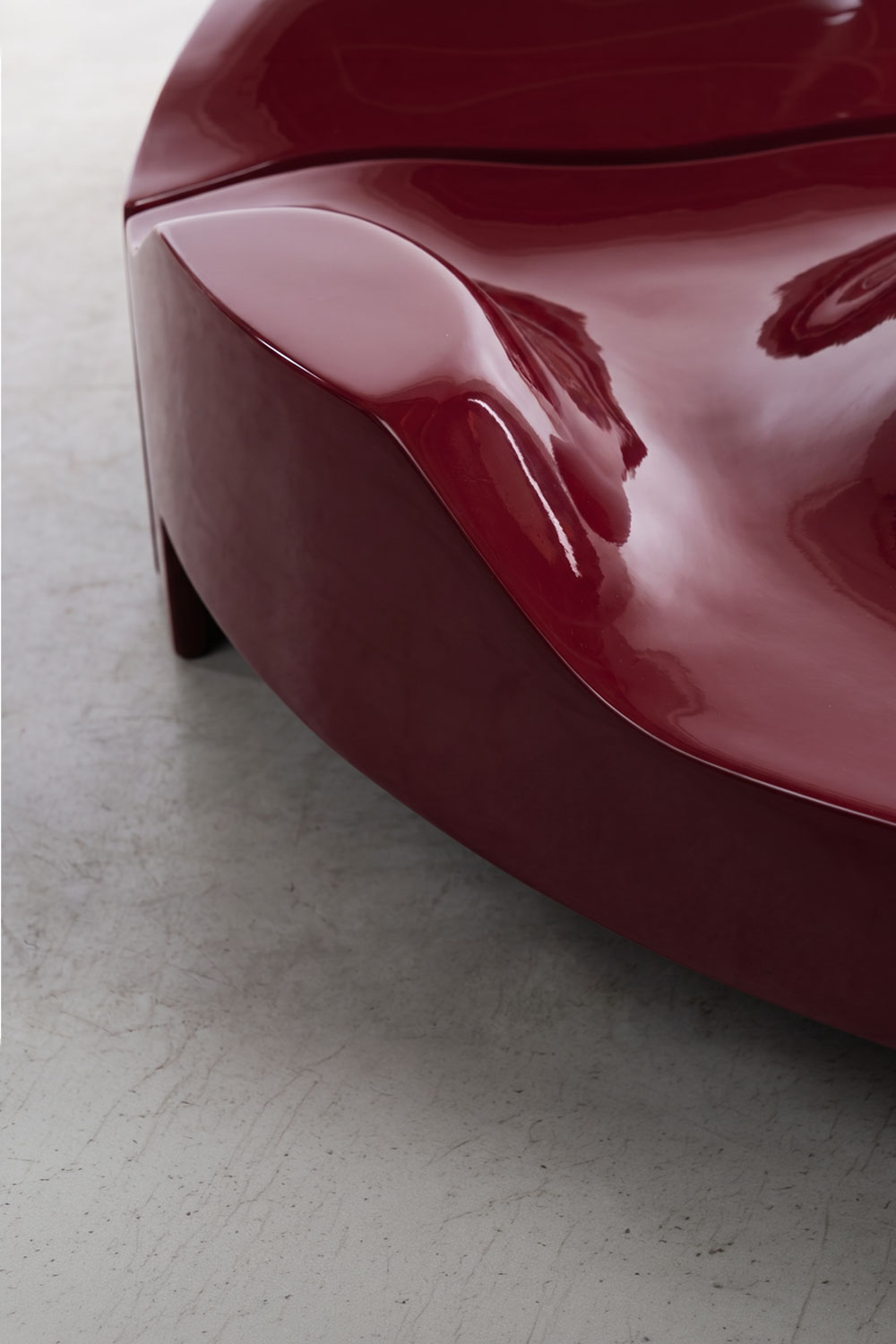 Close-up of the Sun Disc table's high-gloss burgundy edge, curving into a soft dip and reflecting light, with one block leg at the corner.