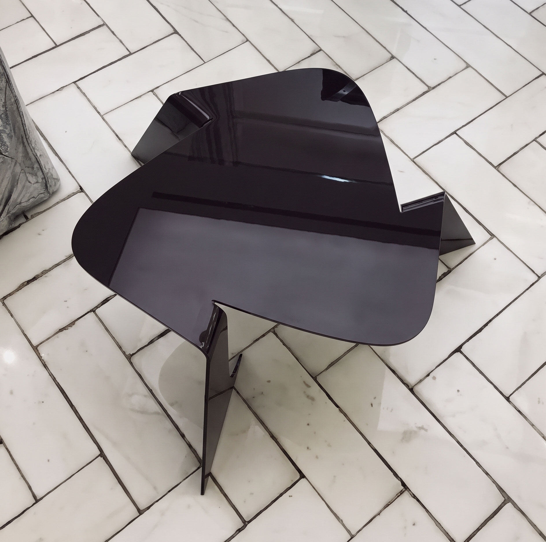 Top view of the Bend table in glossy dark aubergine, with its rounded triangular top and folded legs reflecting a bright interior.