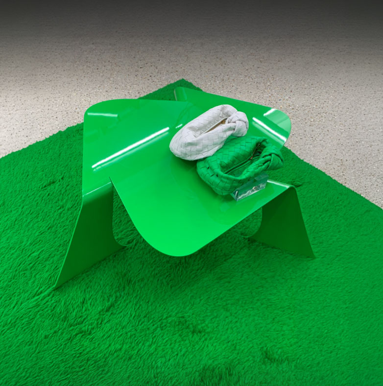 Green Bend table on a bright green shaggy rug, with a white knotted bag and a green woven bag on its top.