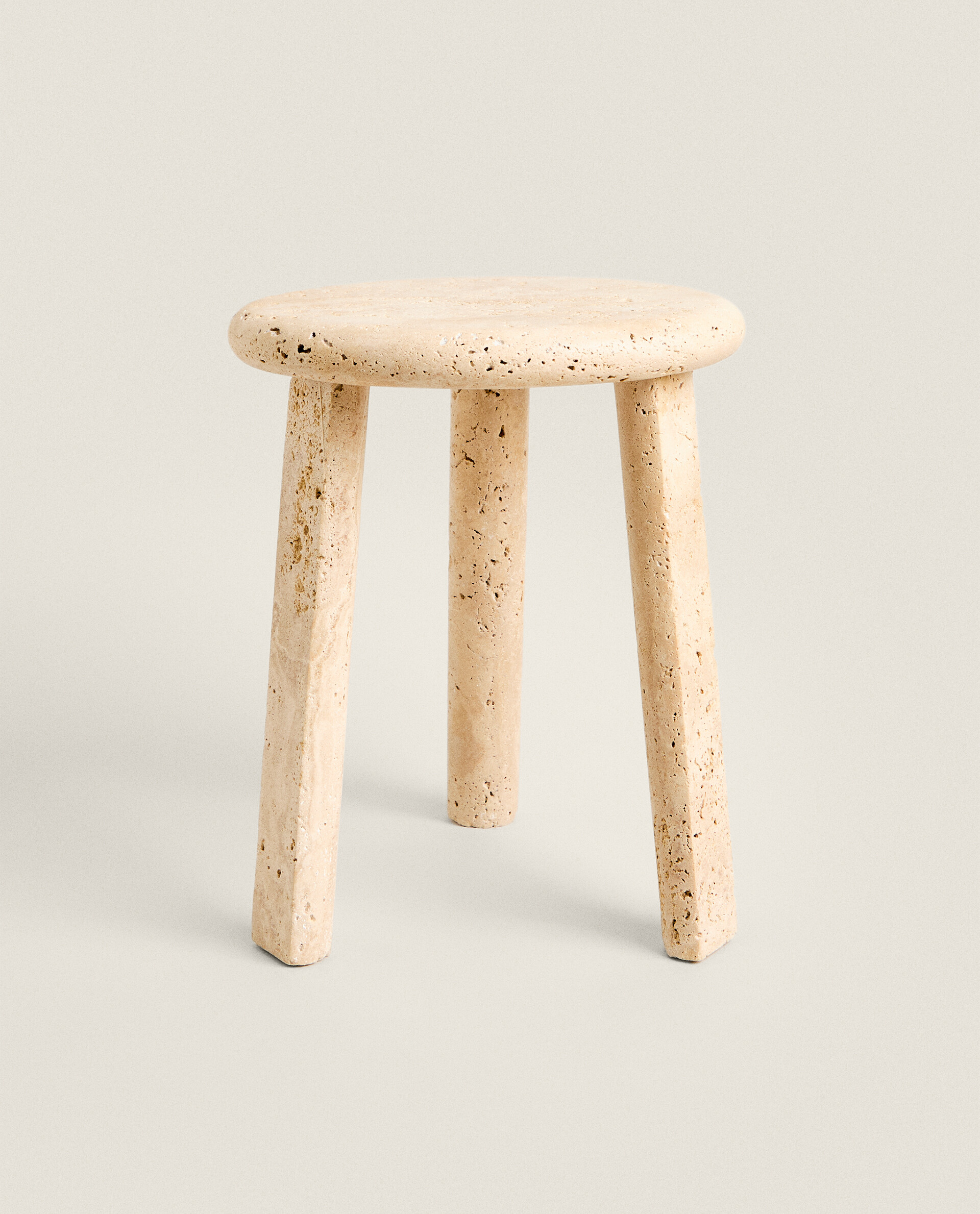 Front view of the Nevada stool: a round, thick top in pale pitted travertine on three slightly splayed legs, against a plain light background