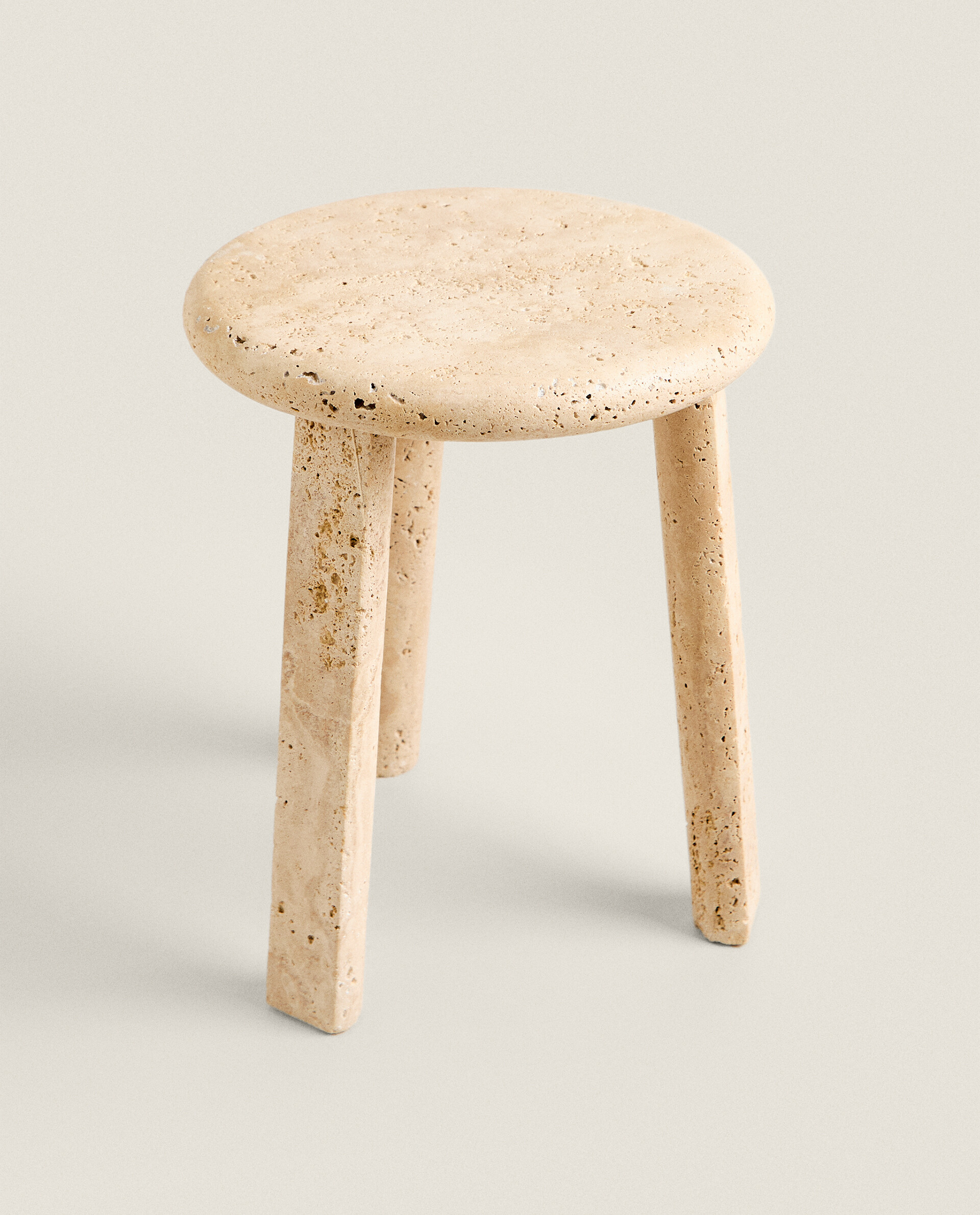 Higher three-quarter view of the Nevada stool, looking down on the round top and its three angular legs, with a soft shadow on a pale floor.