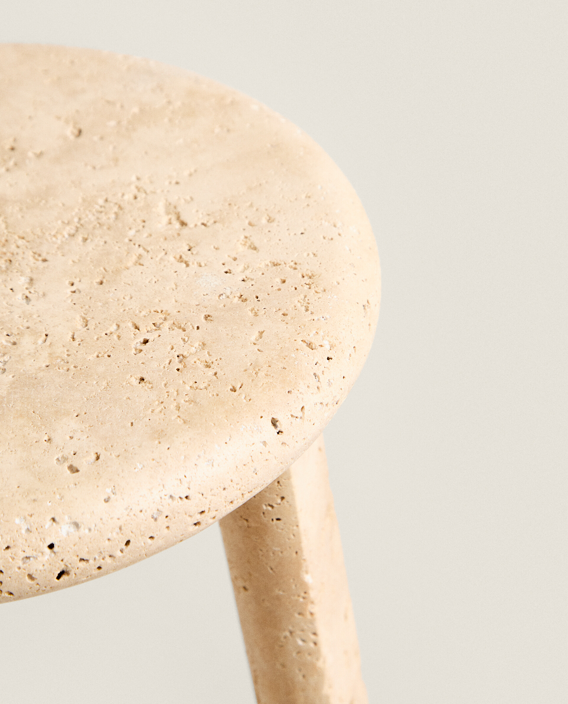 Front view of the Nevada stool: a round, thick top in pale pitted travertine on three slightly splayed legs, against a plain light background
