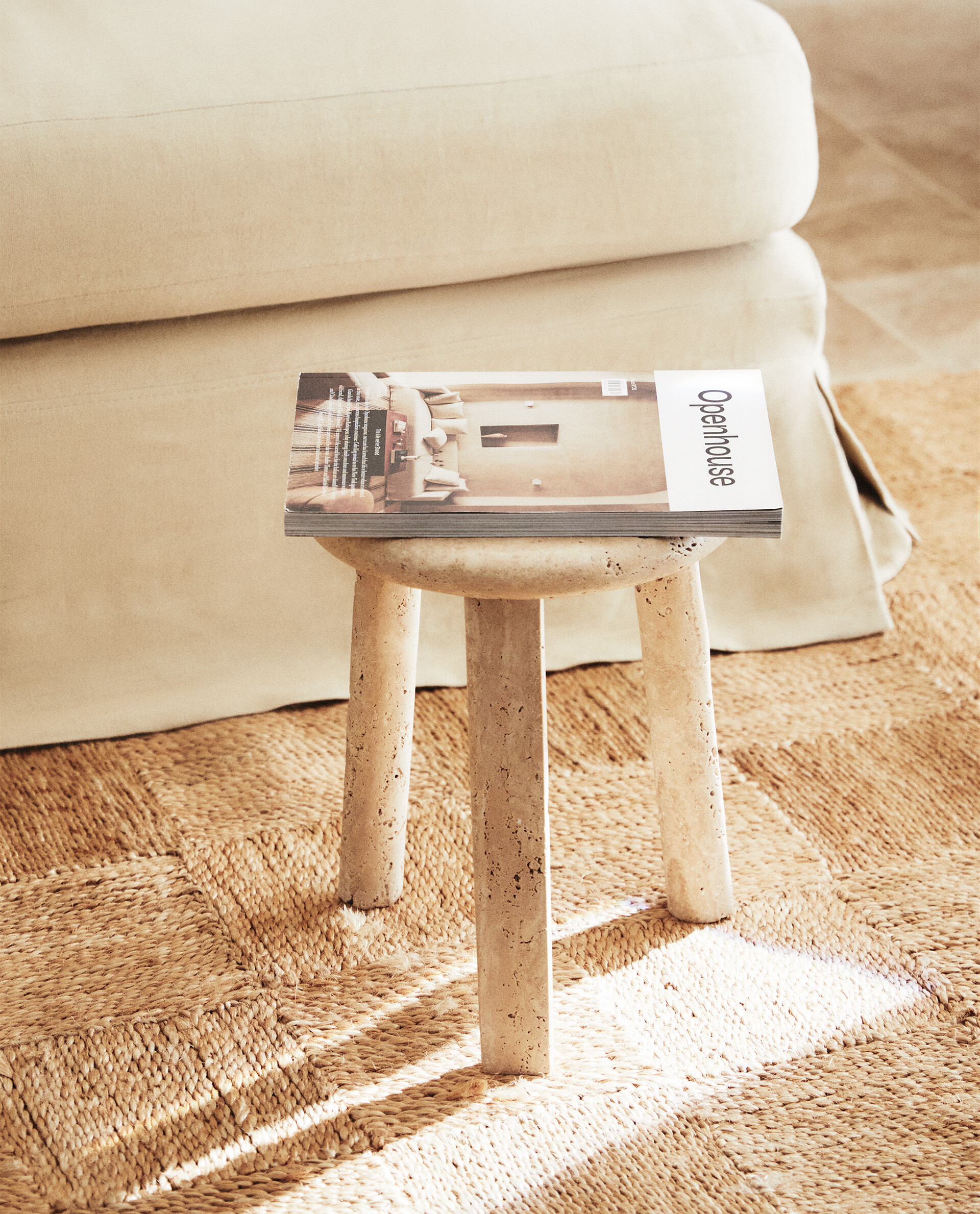 Nevada stool on a woven jute rug in warm sunlight, with a magazine on top and a cream upholstered sofa behind.