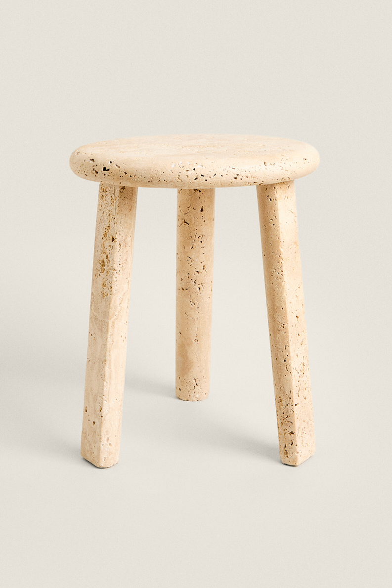 Front view of the Nevada stool: a round, thick top in pale pitted travertine on three slightly splayed legs, against a plain light background.