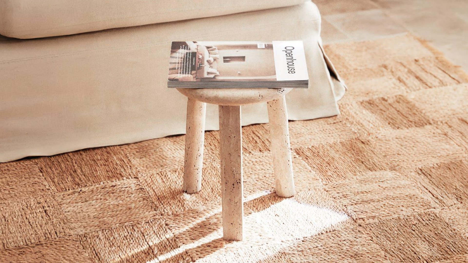 Nevada stool on a woven jute rug in warm sunlight, with a magazine on top and a cream upholstered sofa behind.