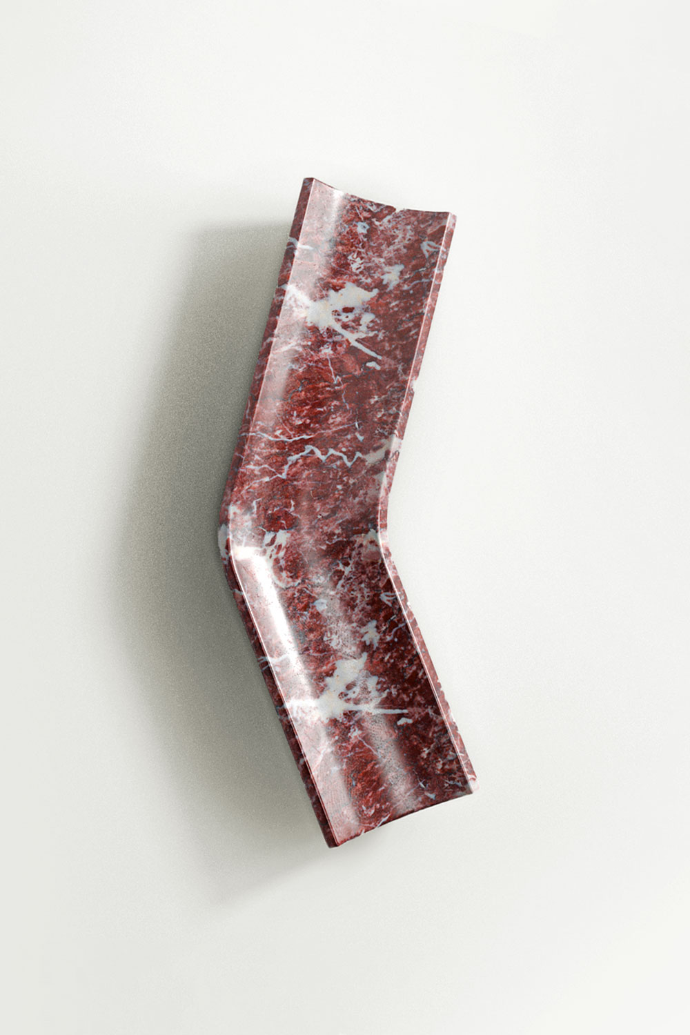 Rosso levanto marble Bow tray with a bent, elongated shape and a slightly raised rim, seen from above against a pale wall.