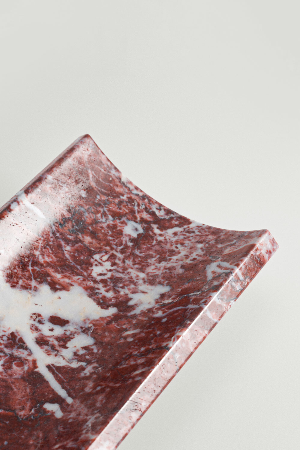 Detail of the rosso levanto marble tray's corner and raised edge, with white veining across the dark red stone.