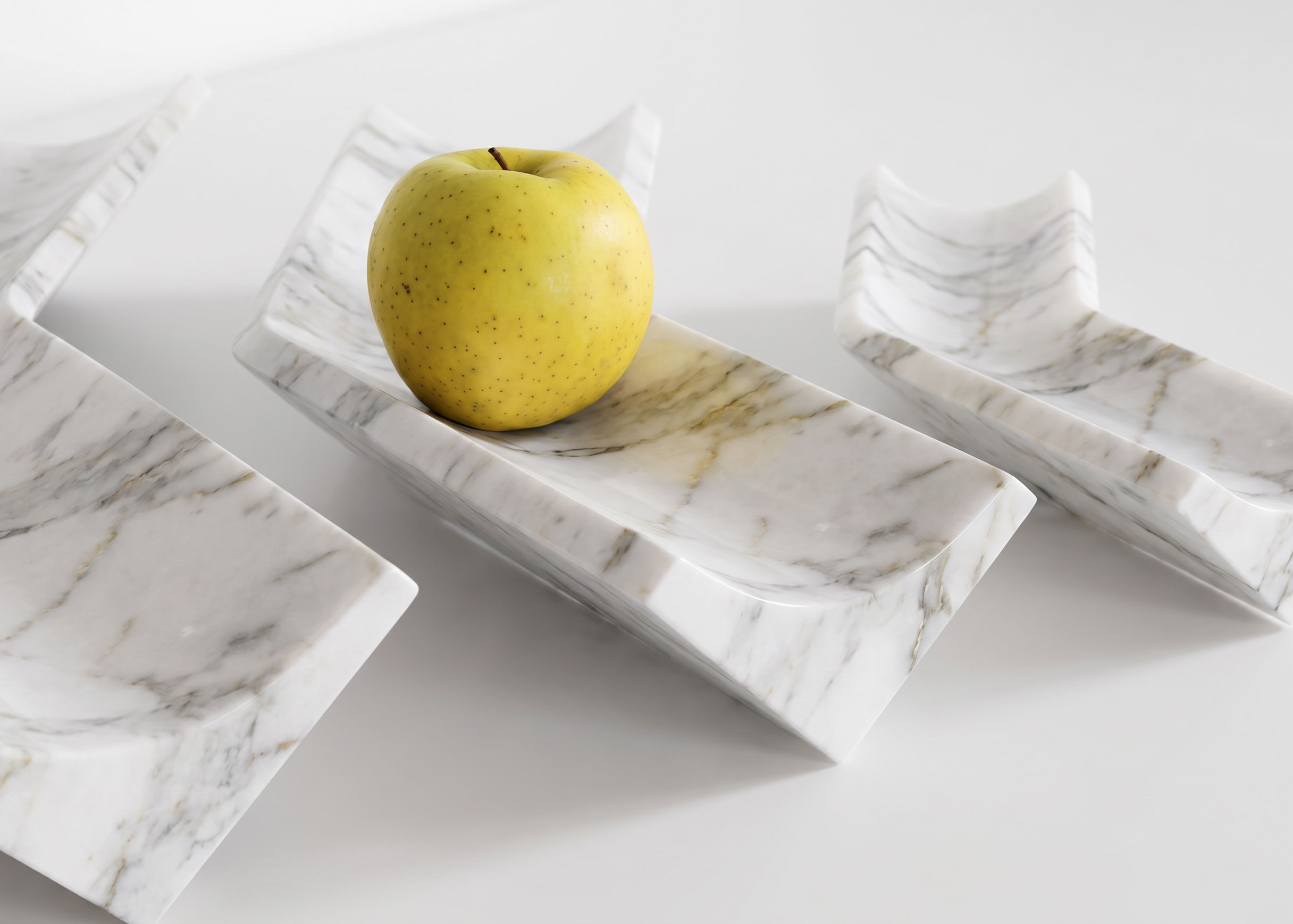 Three white marble Bow trays with a yellow apple resting in the middle tray's curved channel.
