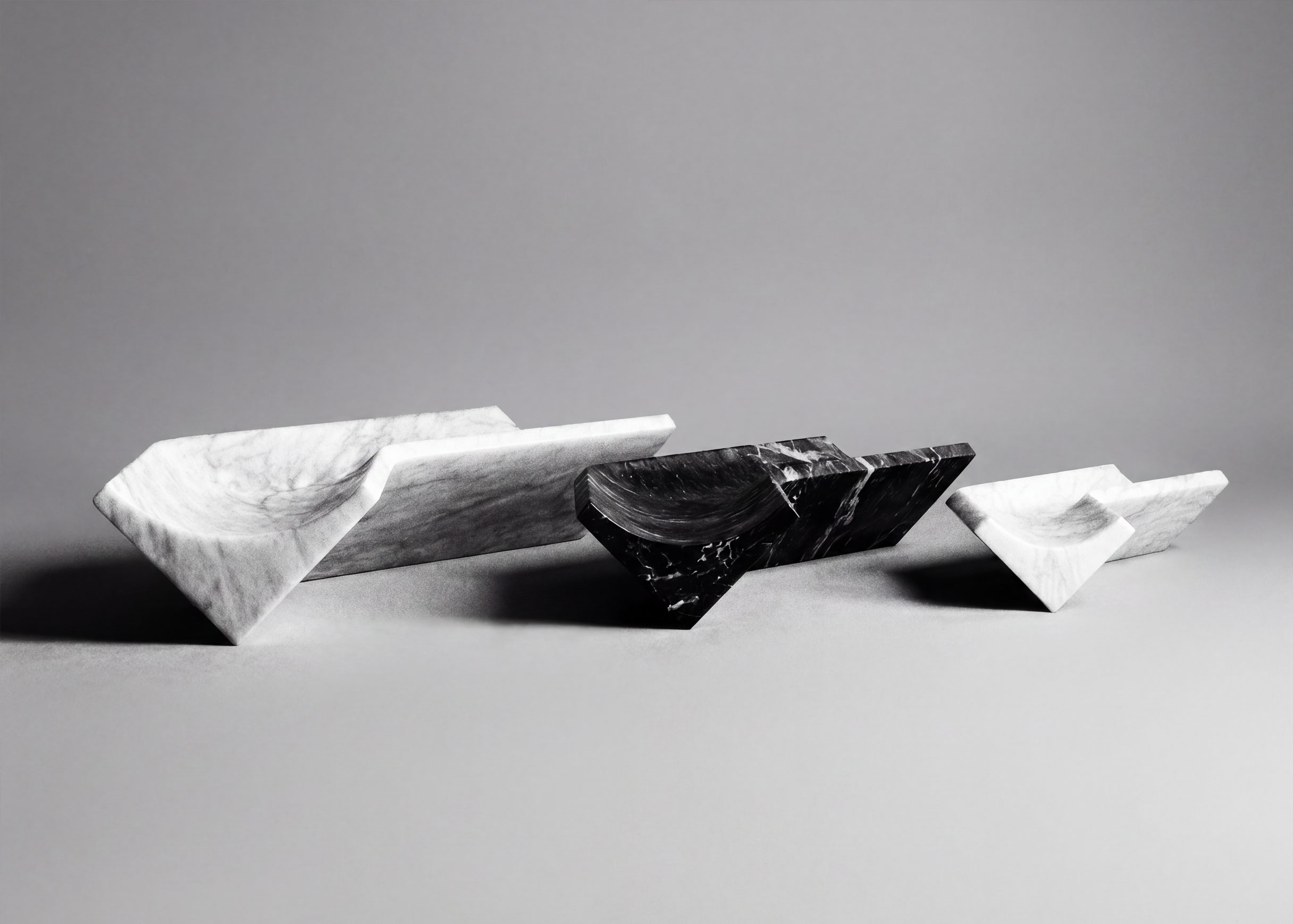 Three Bow trays in a row, in white, black and small white marble, each V-shaped with a curved scoop, in black and white.
