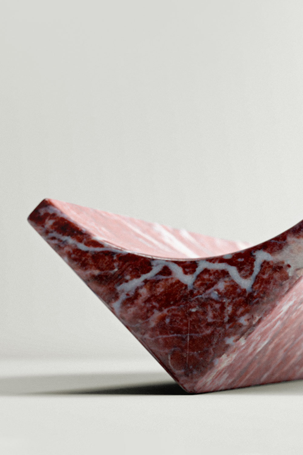 Close-up of a Bow tray in rosso levanto marble with white veins, showing its thick edge and curved scoop.