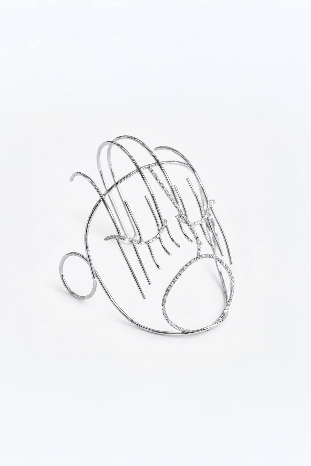 Decorative mask in silver-toned wire, a face outline with vertical rods for lashes, a small ring at one side and eyes and mouth set with small white stones.