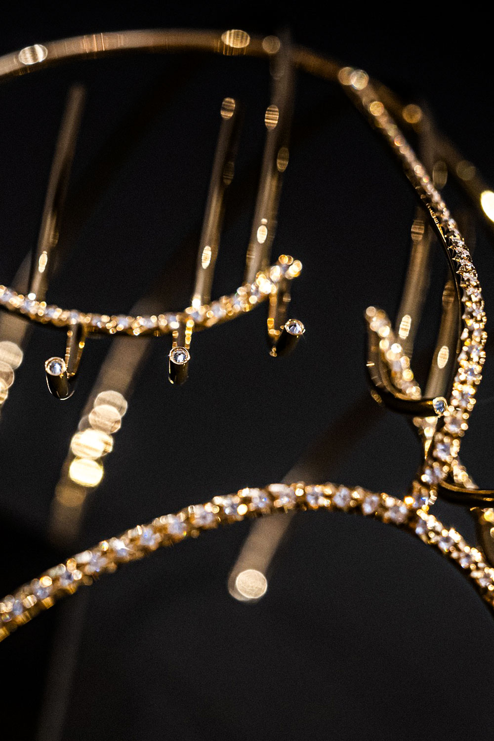 Close-up of gold wire curves set with small white stones, with out-of-focus golden highlights on a dark background.
