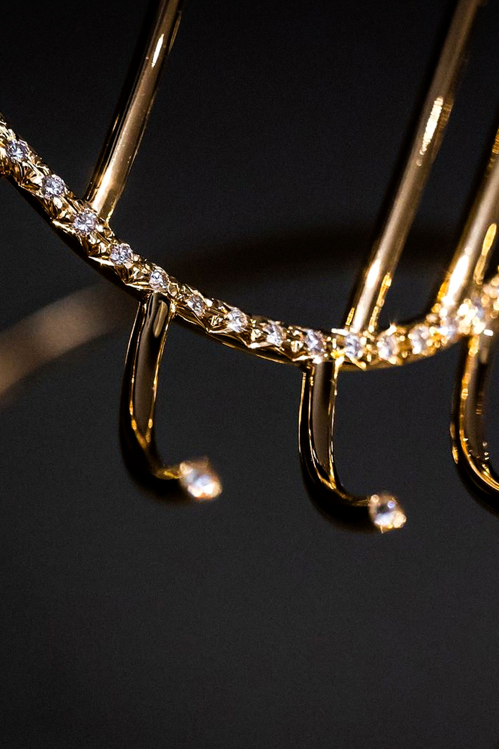 Close-up of gold rods with curled tips, each tip set with a small white stone, below a curved line of stones.