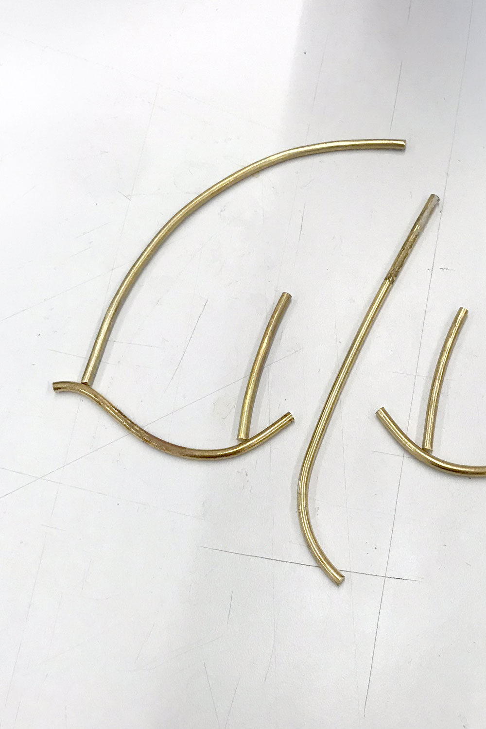 Loose curved gold-coloured metal rods on a white worktop, the separate parts of a mask before it is assembled.
