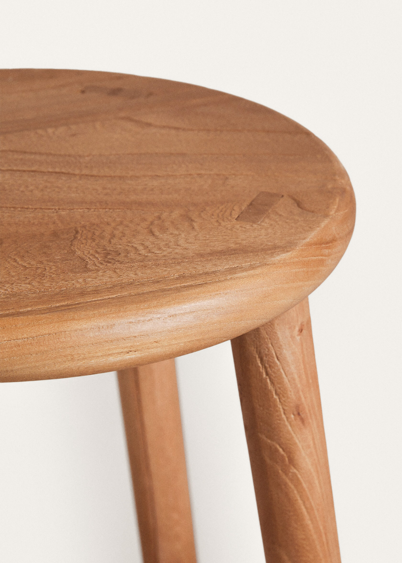 Close-up of the Teide stool's round top, showing its softly rounded edge, flowing grain and a small rectangular wooden joint.