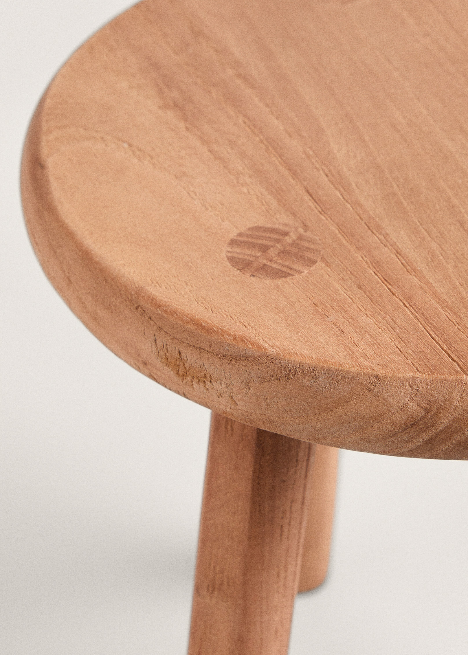 Close-up of the Teide stool's round top, showing its softly rounded edge, flowing grain and a small rectangular wooden joint.