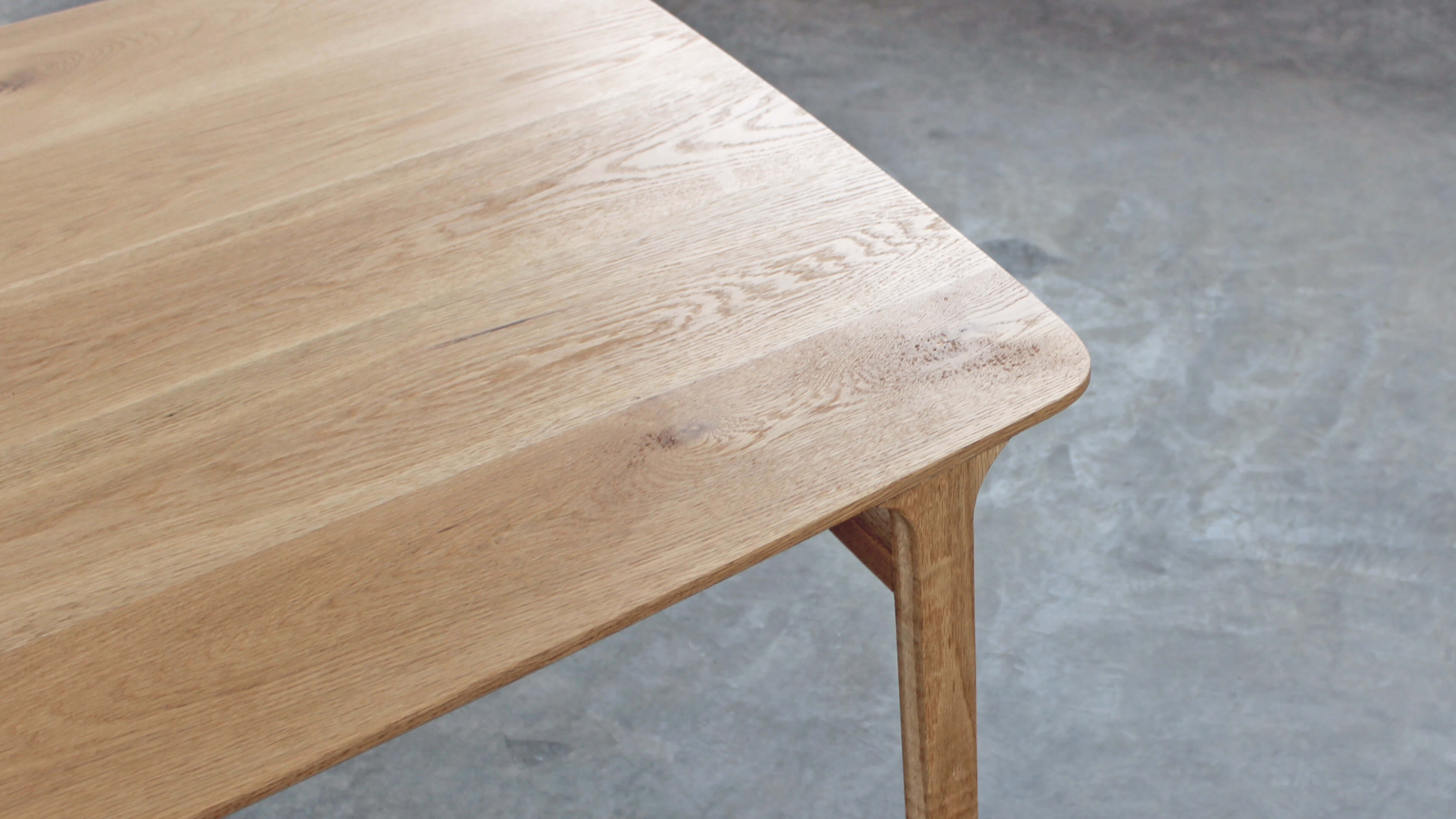 Top view of the oak tabletop and its rounded corner, with wide boards, visible grain and a leg curving up at the edge.