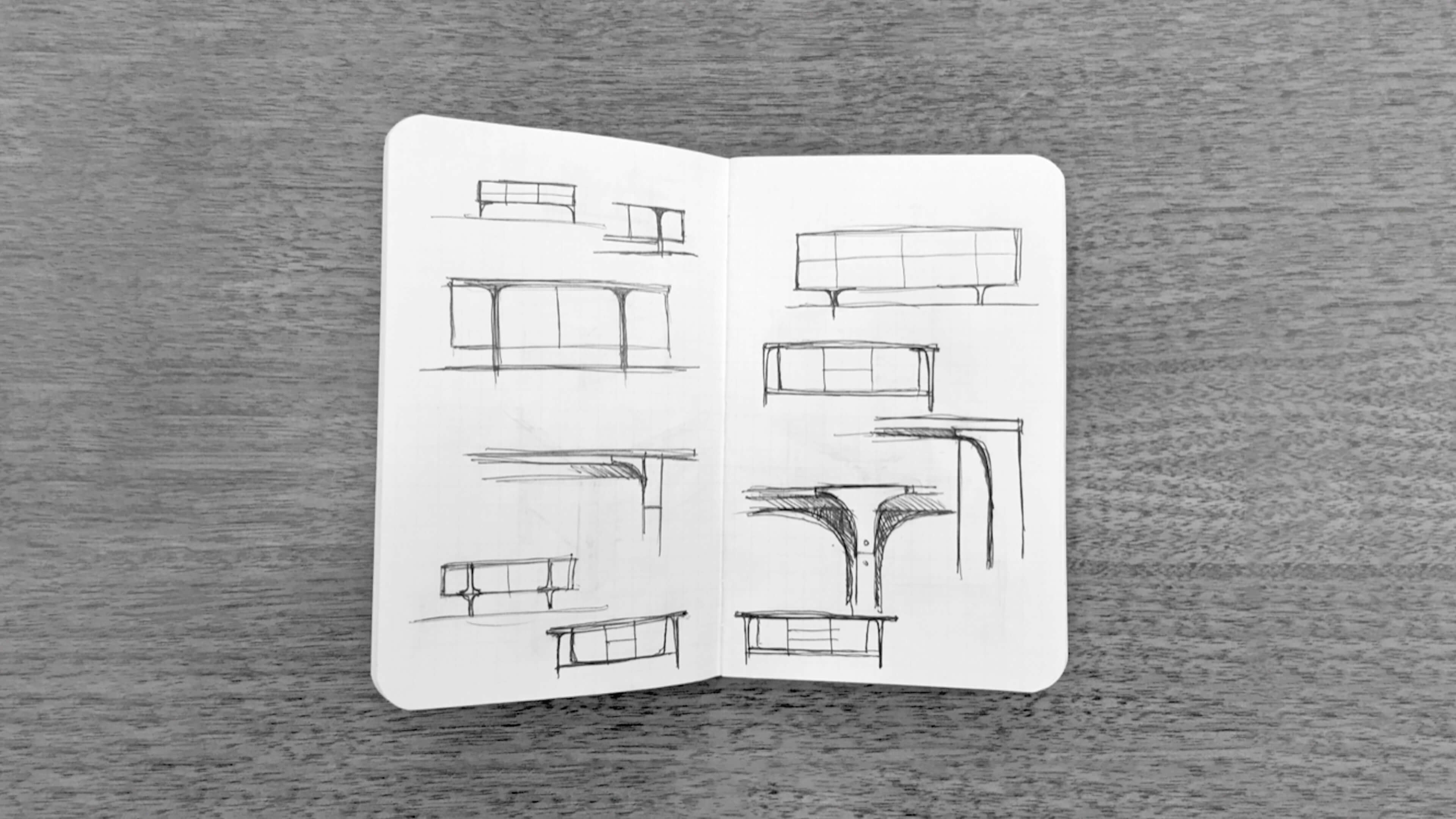Open sketchbook on a dark wood surface, with pen sketches of low tables and sideboards on slender legs, and details of their curved leg joints.