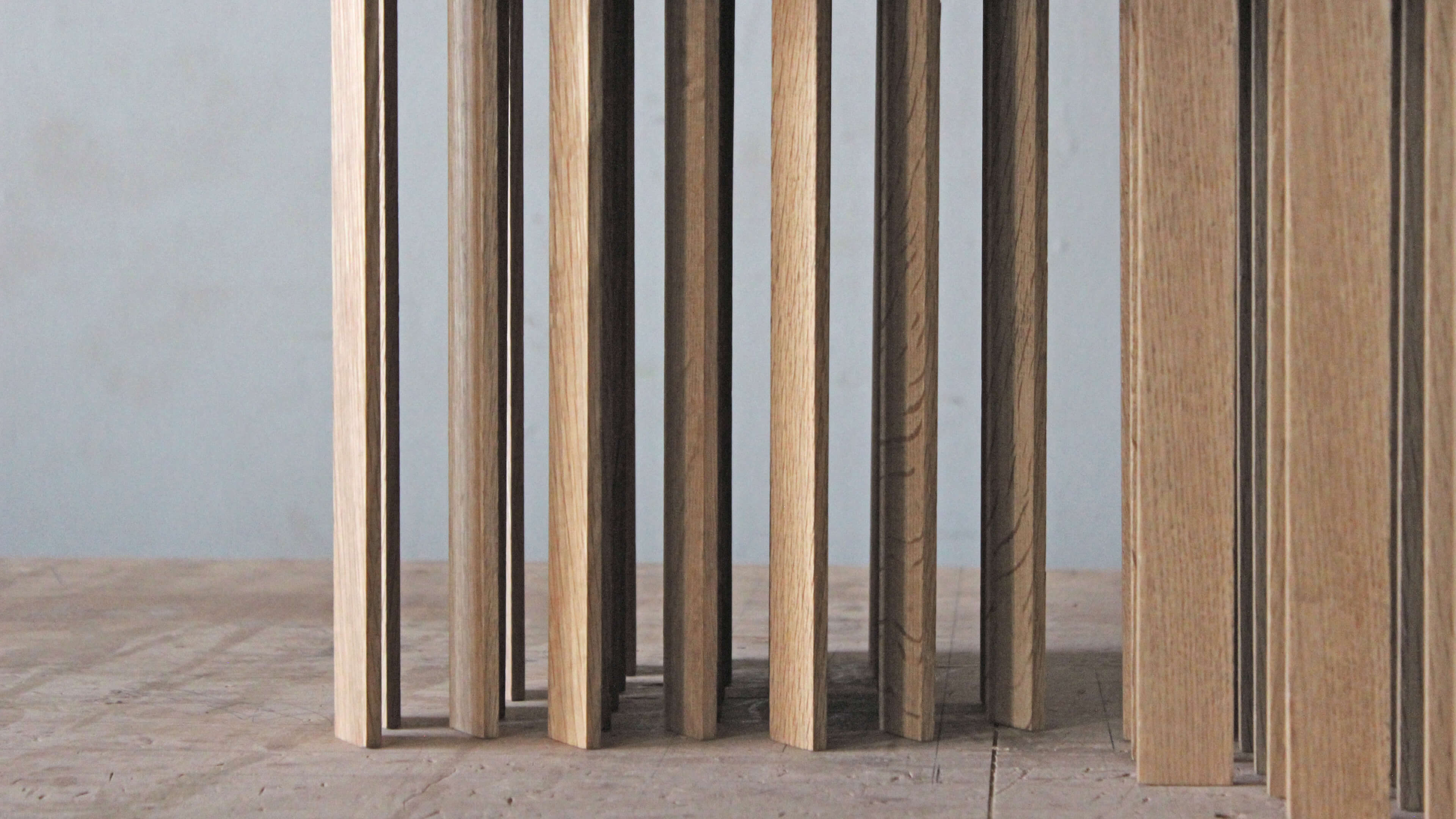 Close-up of the table's oak slat legs standing in rows, with the grain visible and the grey wall behind.