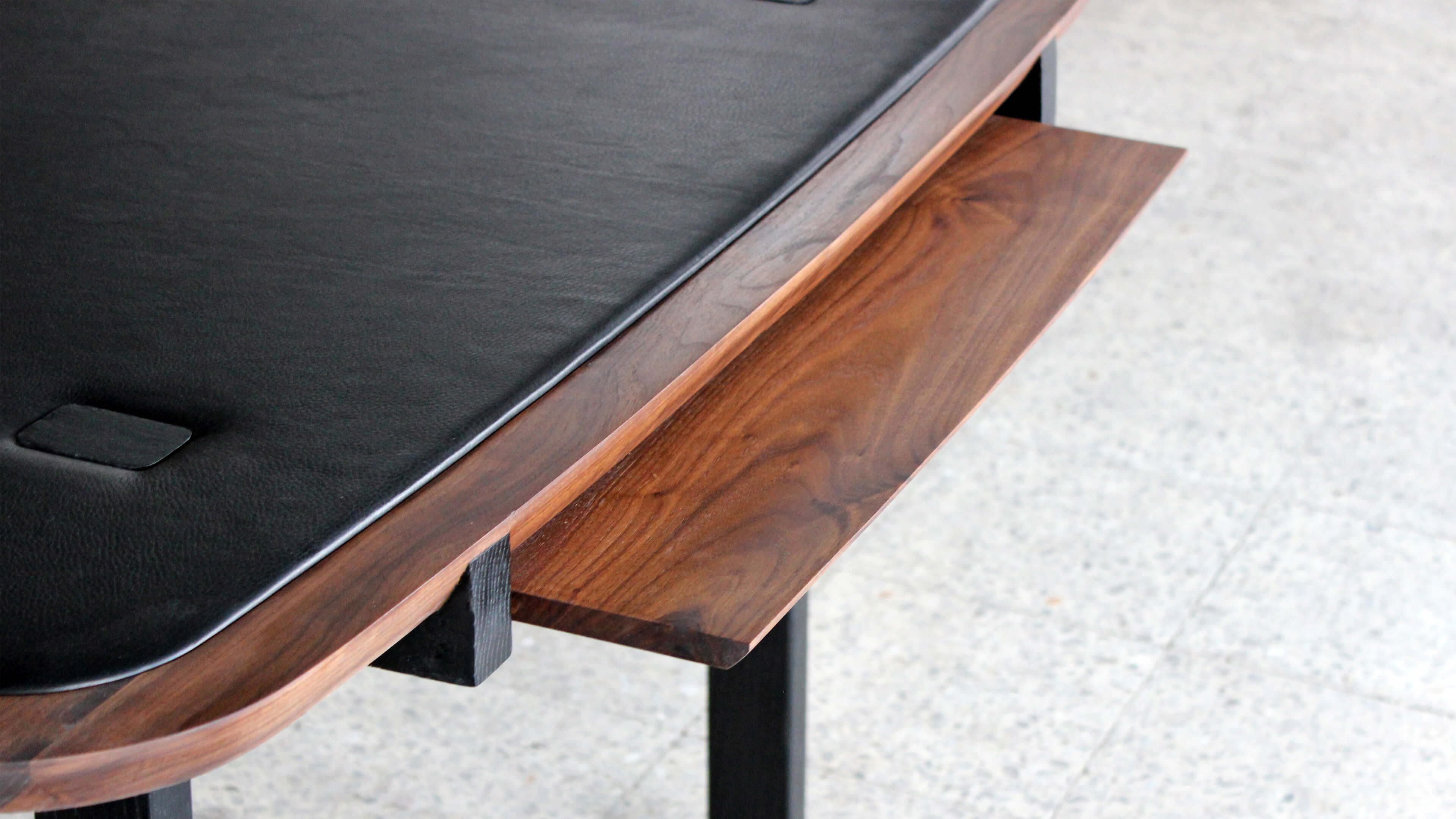 Close-up of a sliding walnut tray beneath the leather top, showing its grain and the black support behind.