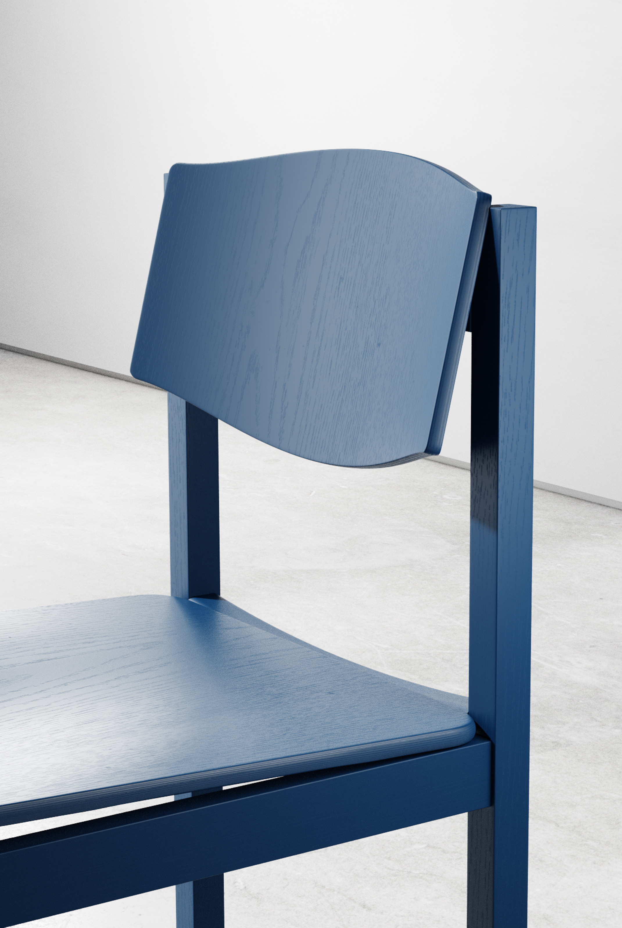 Side detail of the blue chair, with the curved backrest panel, the dished seat and the square frame, in soft daylight.