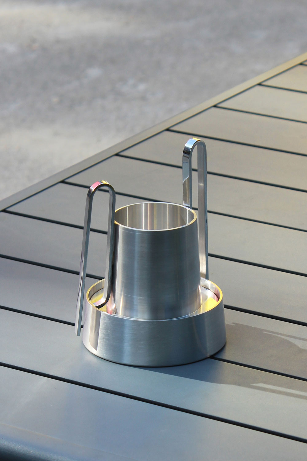 Bloom on a grey slatted outdoor table, with its conical base, tapered upper vessel and two upright loop handles catching the light.