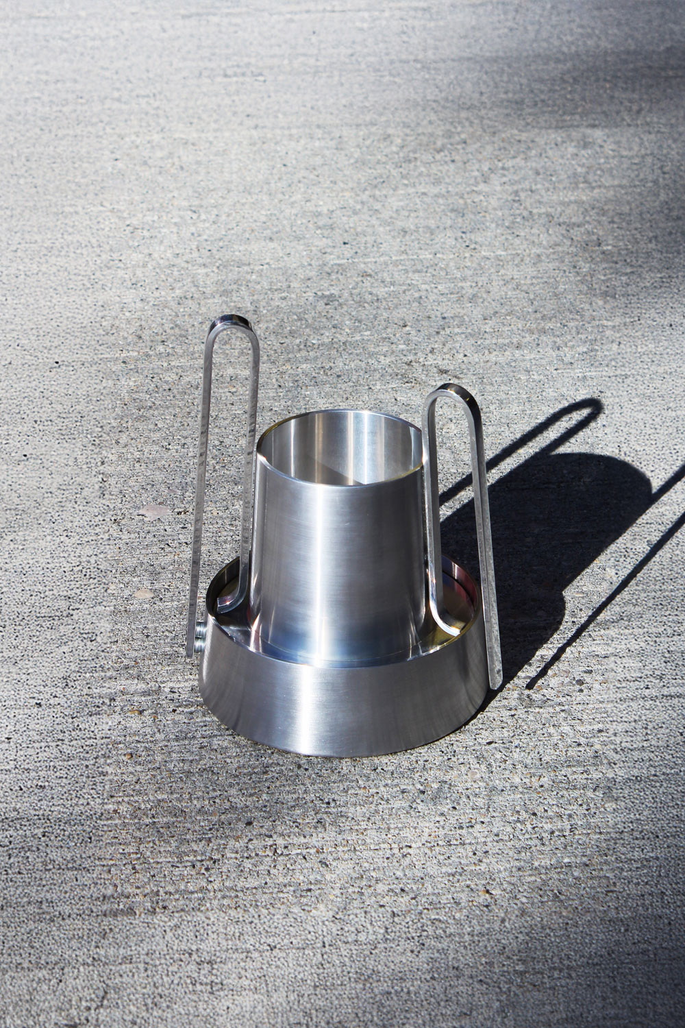 Bloom on concrete in strong sunlight, with the two loop handles rising on either side of the polished vessel.