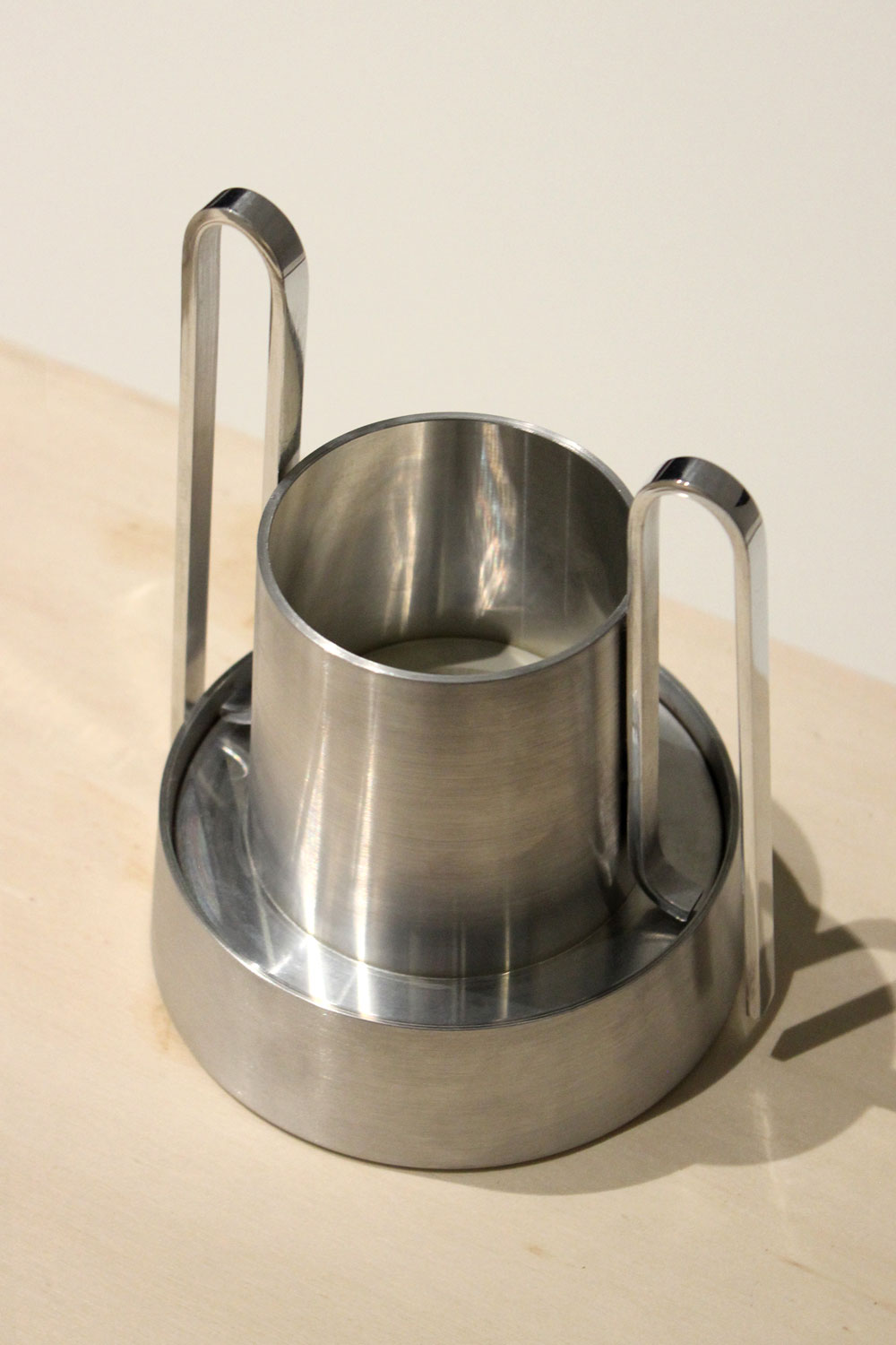 Bloom on a light wooden surface in front of a cream wall, with its curved handles and polished base ring.