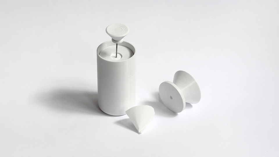 White prototype parts for the dripper: a cylinder holding a thin rod topped with a ribbed disc, a spool-shaped cone and a folded paper filter.