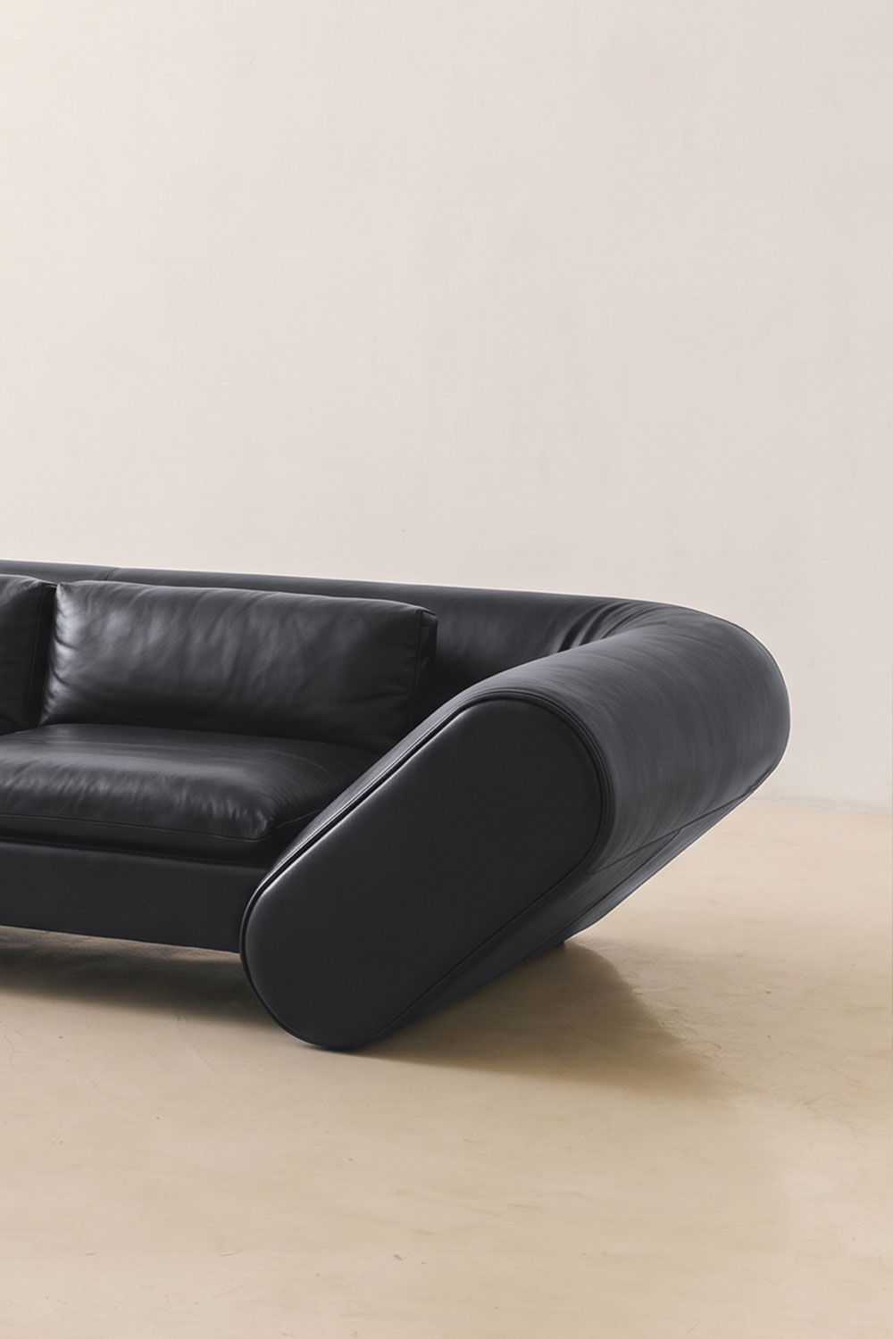 Close-up of the Lee sofa's rounded black leather armrest and a back cushion, on a pale floor.