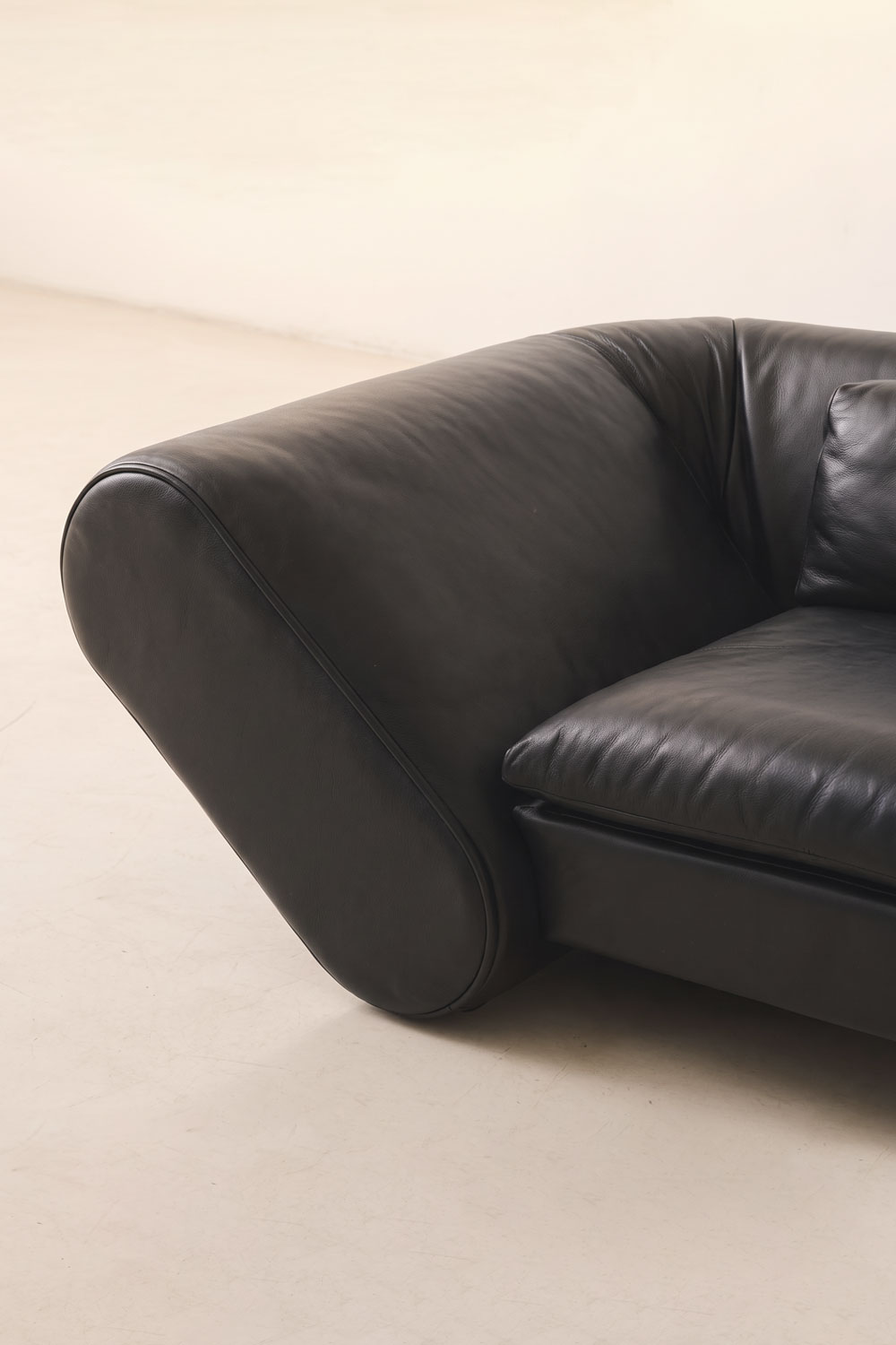 Detail of the black leather armrest seen from the front, with the seat cushion and seam stitching.