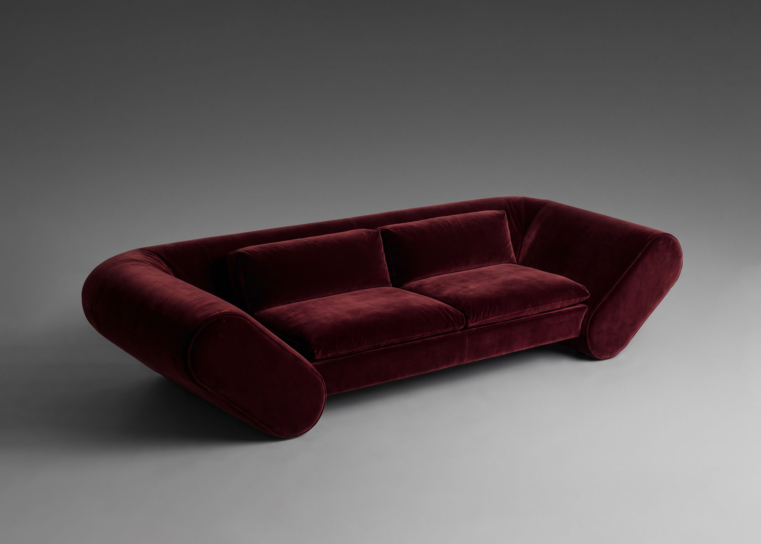 Lee sofa upholstered in deep burgundy velvet, seen from above at an angle against a grey backdrop.