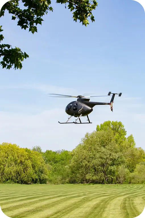 Velvet Ride-branded helicopter landing in an open field near a scenic Irish estate, offering luxurious point-to-point transport.