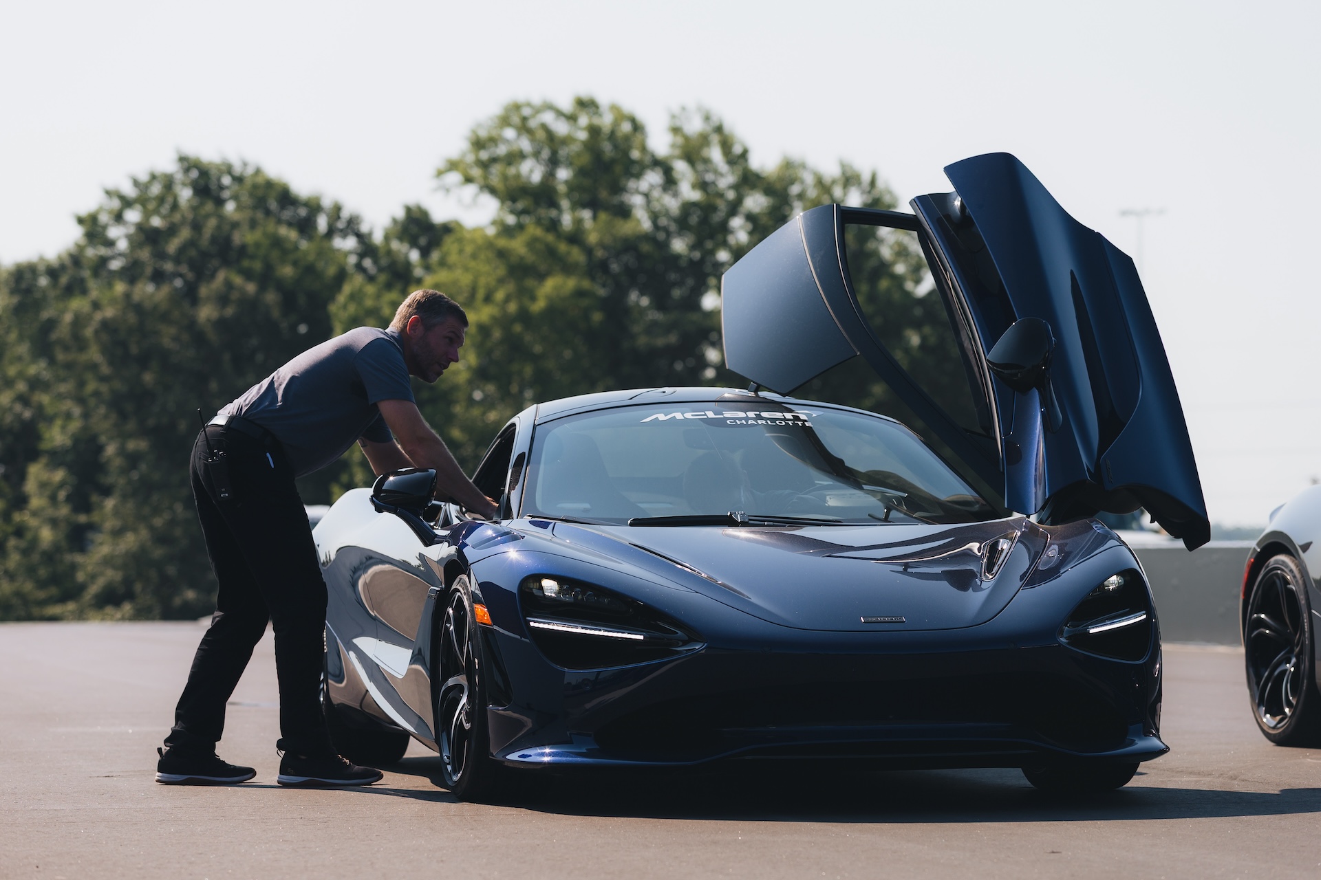 Man leaning into the driver's seat of a dark blue McLaren sports car with its butterfly door open.