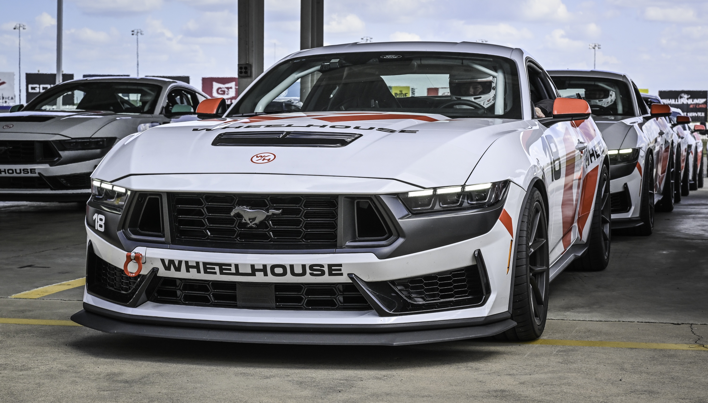 Three people wearing blue shirts cleaning the windshield of a blue McLaren sports car outdoors.