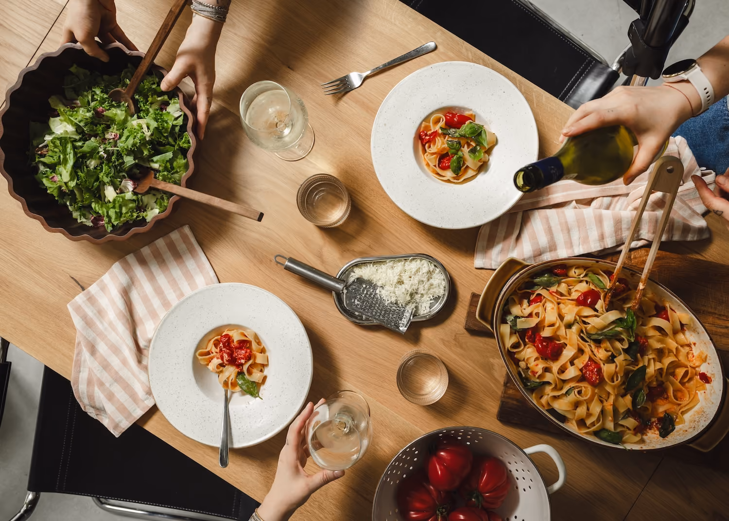 Oak HOOM table during a shared meal, with pasta, salad and wine