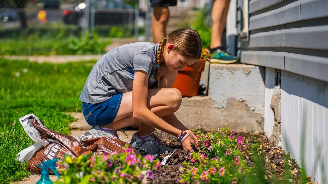 A woman kneeling down to plant some flowers.