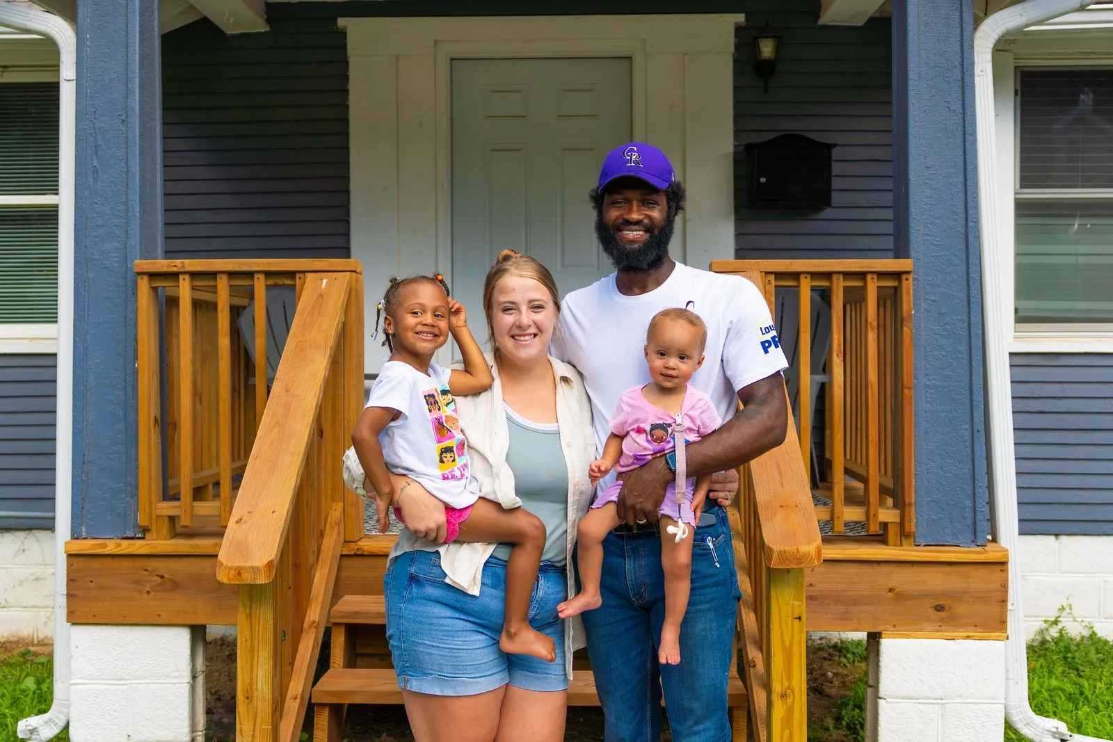 A man, woman and two children standing in front of a house.