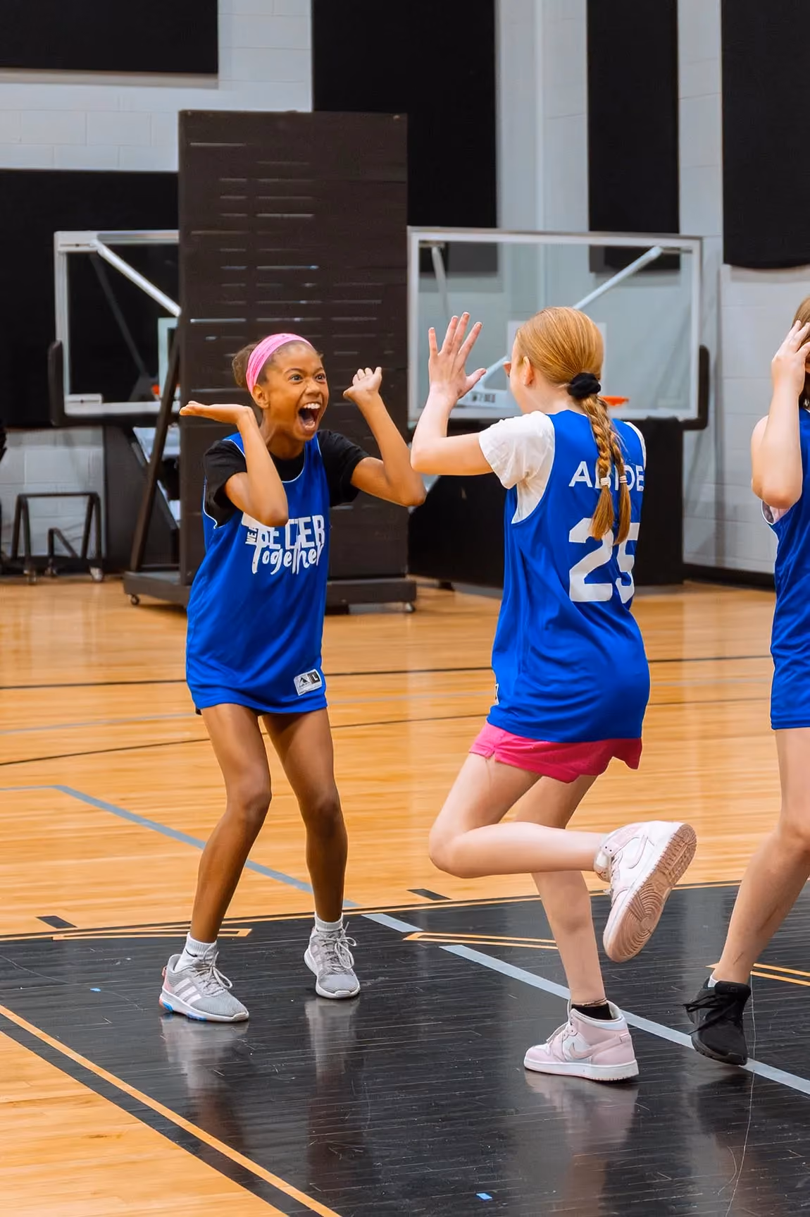 Two girls in Abide jerseys celebrate with a high five on the basketball court.