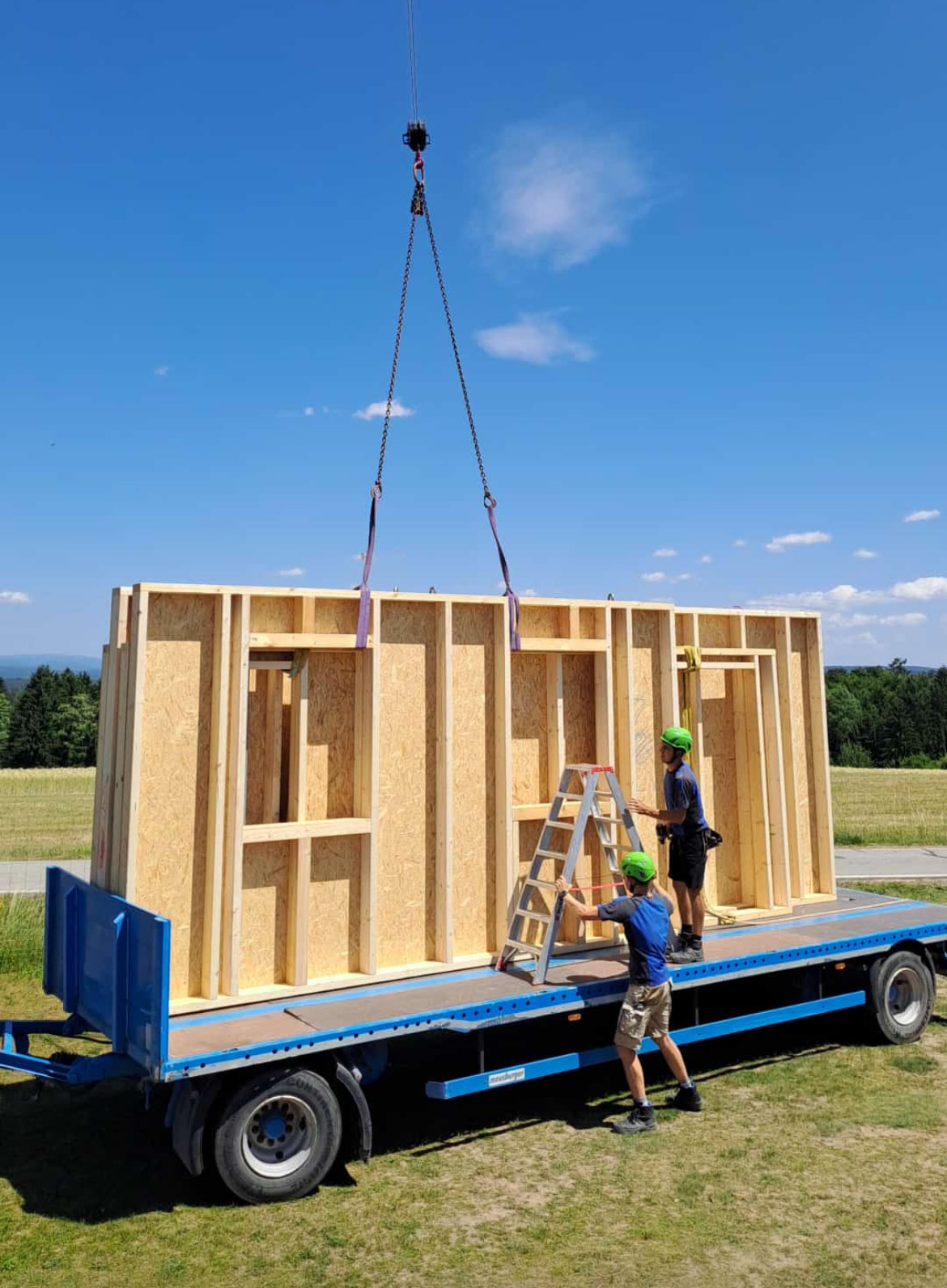 Es ist ein offener Anhänger zu sehen auf dem Wände eines Holzhauses verladen werden.